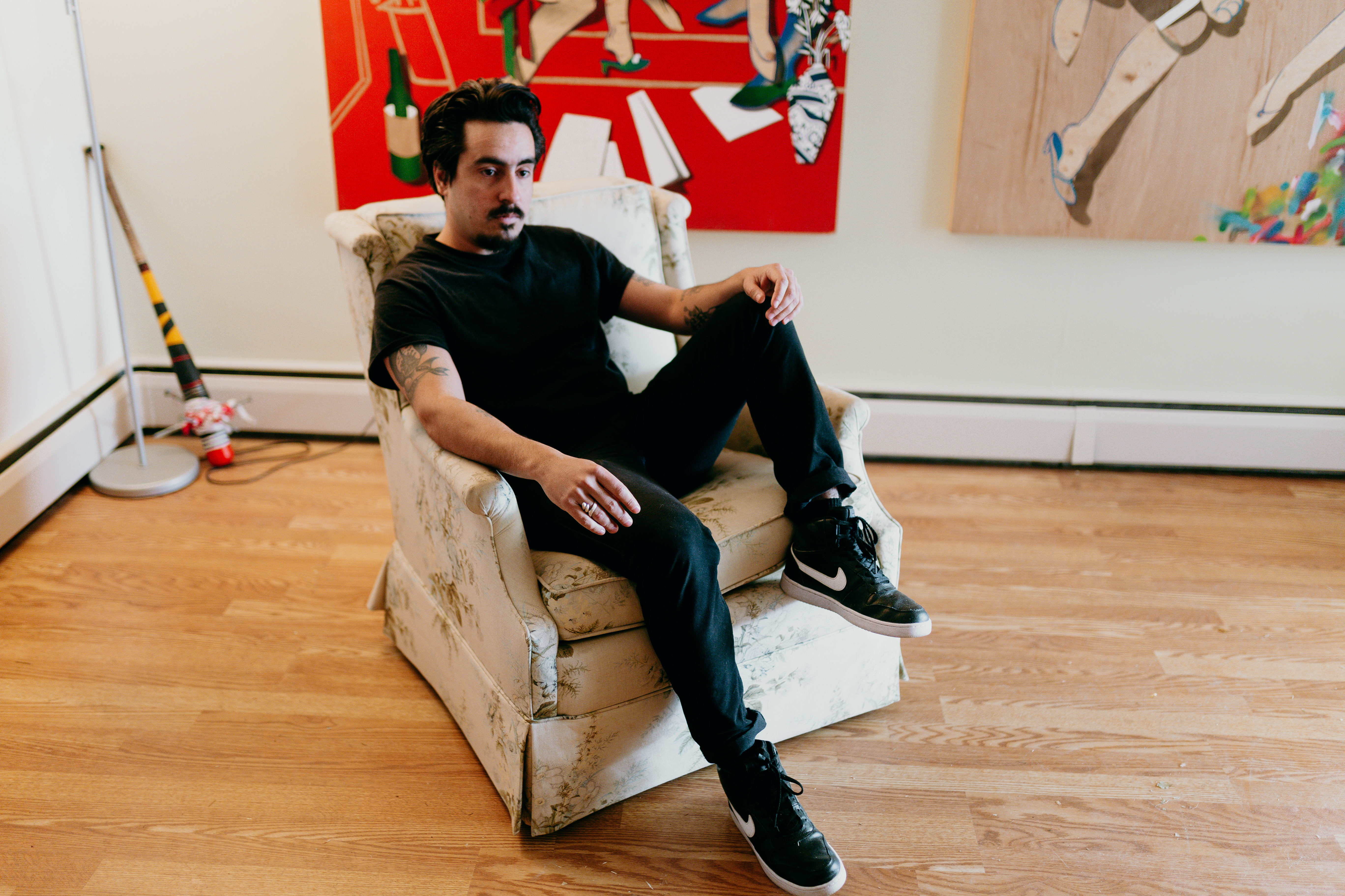 A man in all black sits on a couch in an indoor space. 