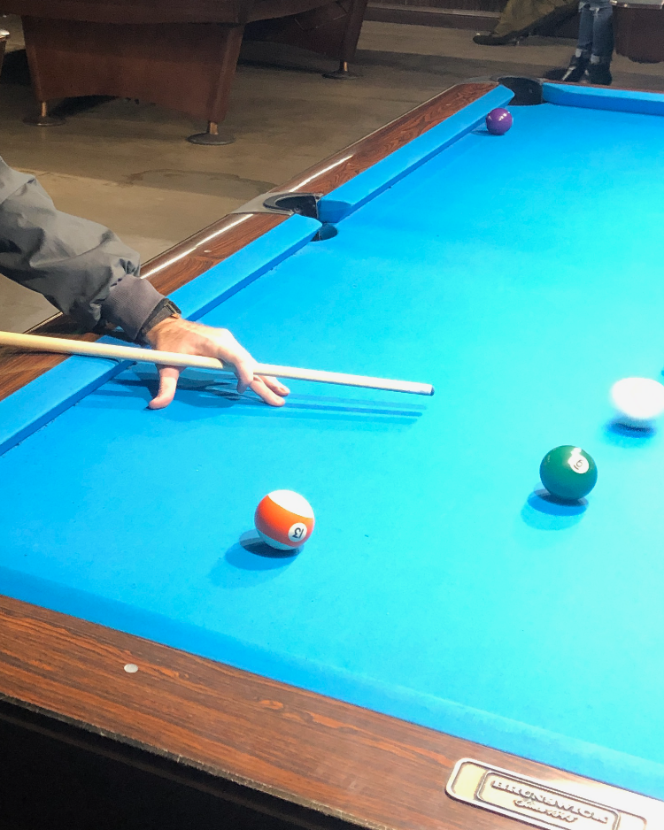 A hand is holding a cue stick above a billiards table about to strike the cue ball.