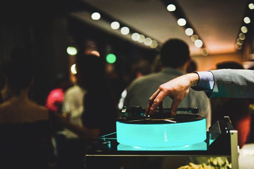 A suited hand spins a vinyl in a bar setting. 
