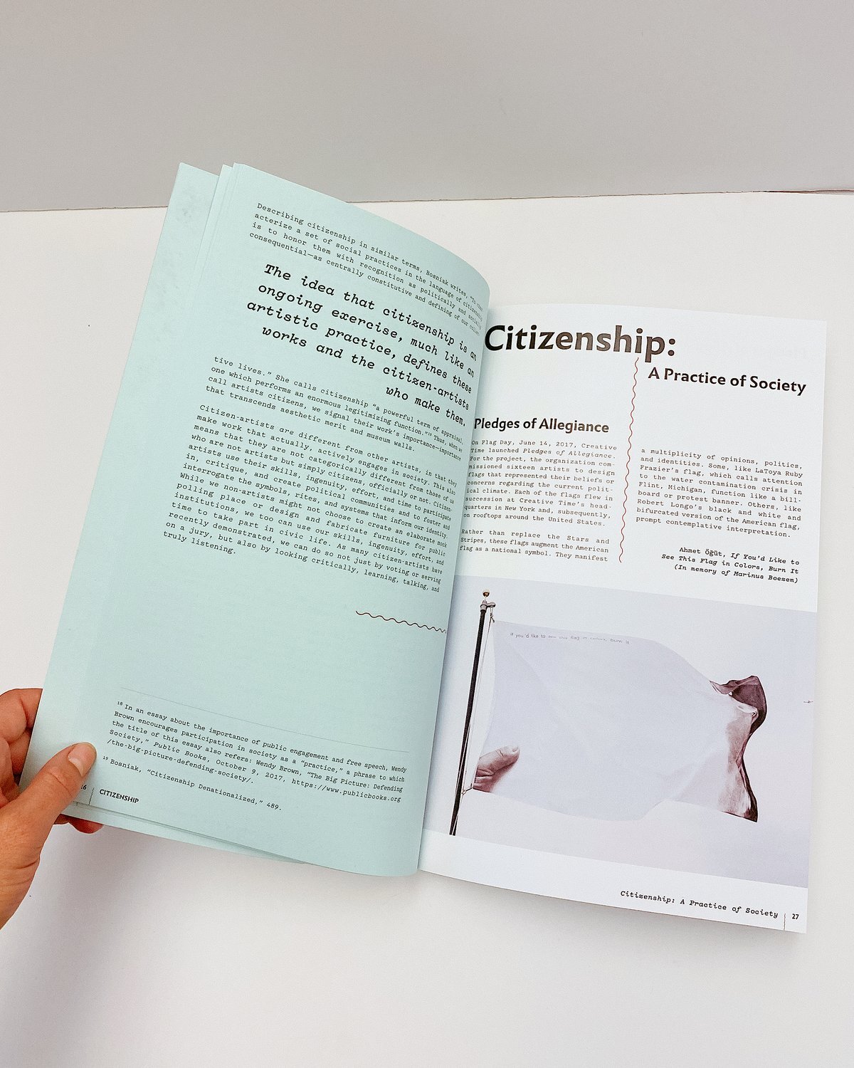 Image of an open Citizenship catalogue, on the left side is teal page with text and on the right page is a white page with text and an image of a flag. The catalogue is held open by a white hand on the bottom left.