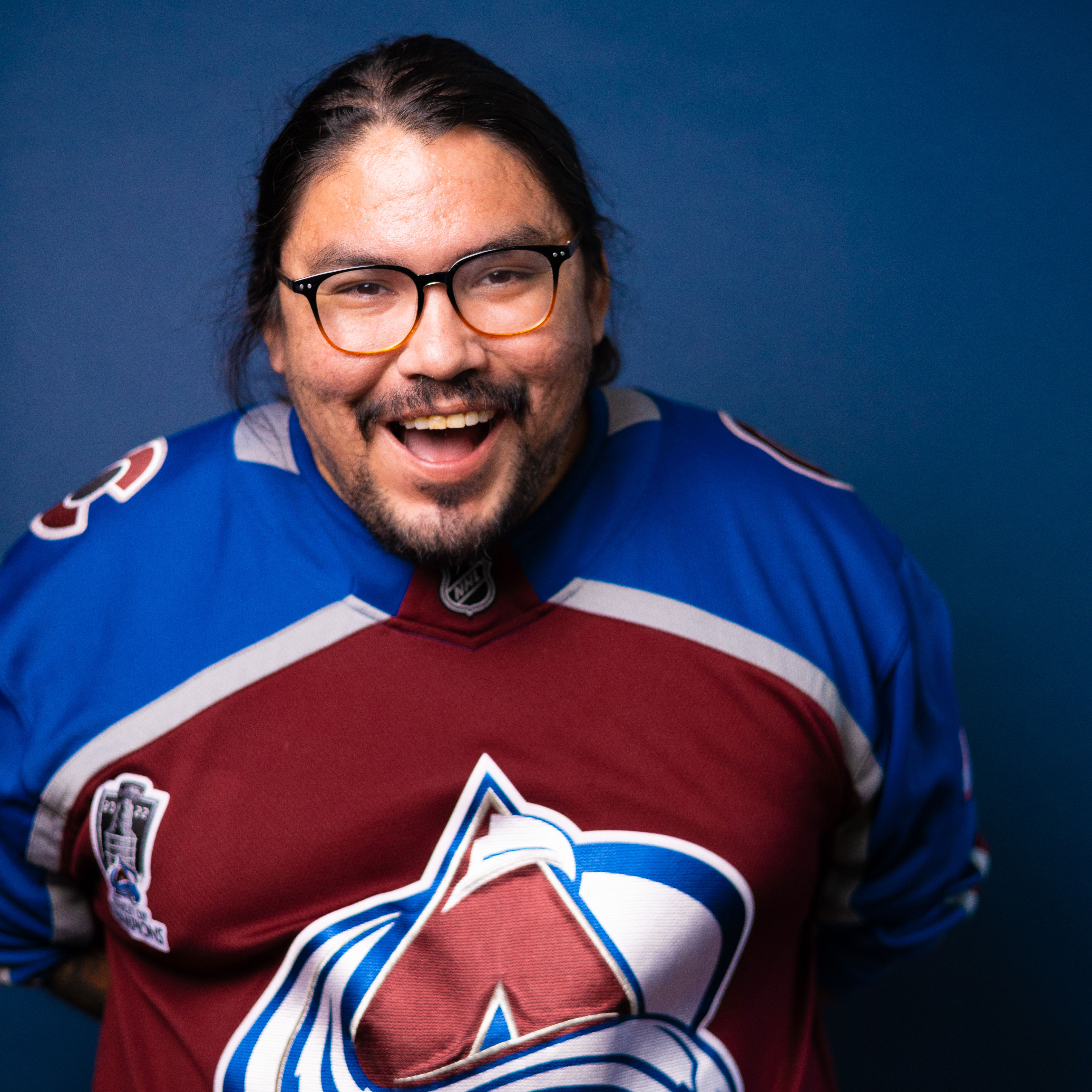 Joshua Emerson sporting an avs jersey and smiling big.