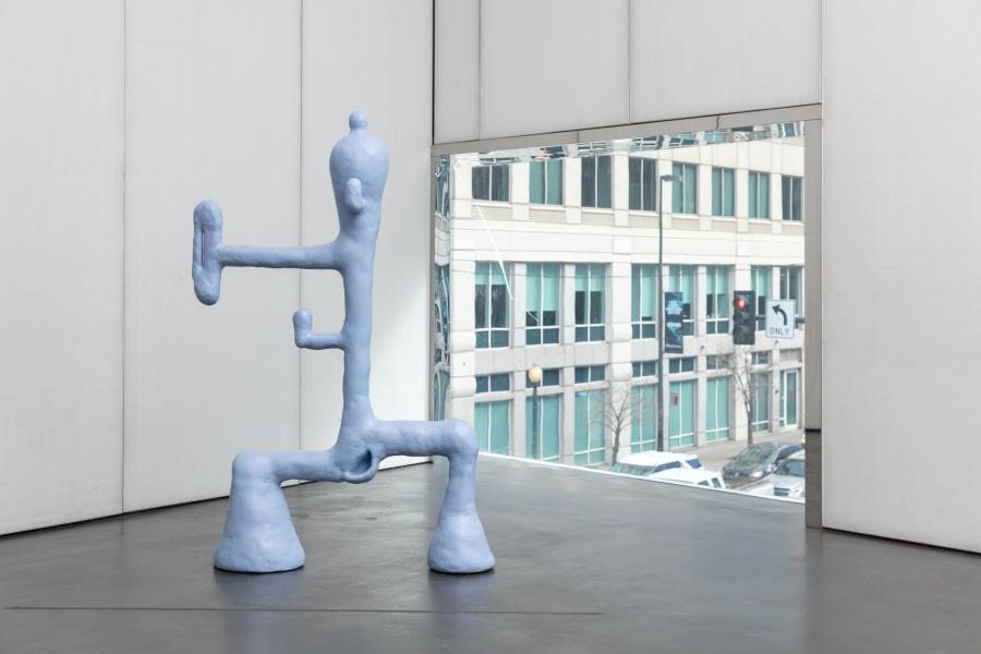 Light blue metal, plaster, epoxy clay, and enamel artwork that looks somewhat like a big industrial pipe. The sculpture is positioned next to a window.