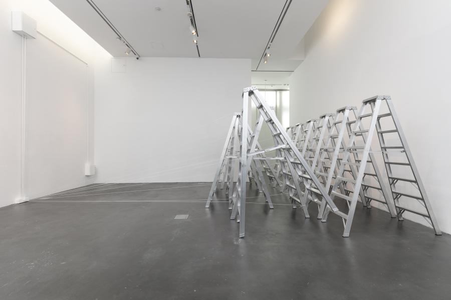 Two rows of silver ladders in an MCA Denver gallery. String-like material attached the ladders to a nearby wall.