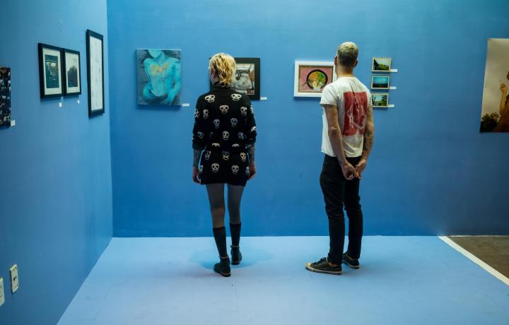 Two teens looking at artwork hung on a blue wall. 