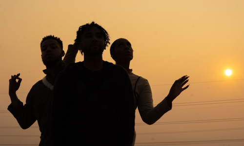 photo of the band. Silhouette of the band with a burning orange glow from the sunset behind them