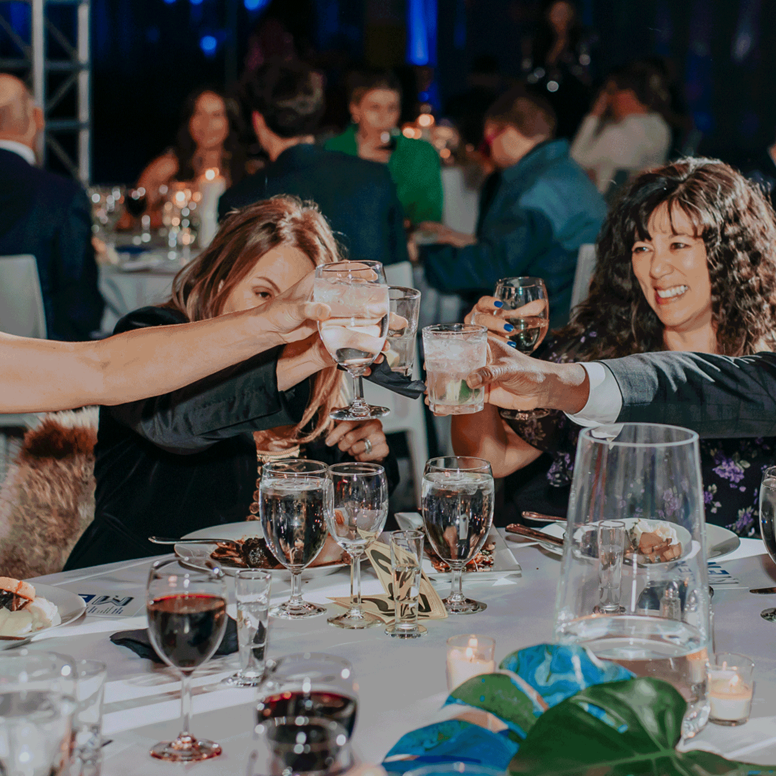 Rotating images captured at a gala: people raising their glasses, lettered balloons, a DJ cast under a red hue, and a warehouse displaying artwork.