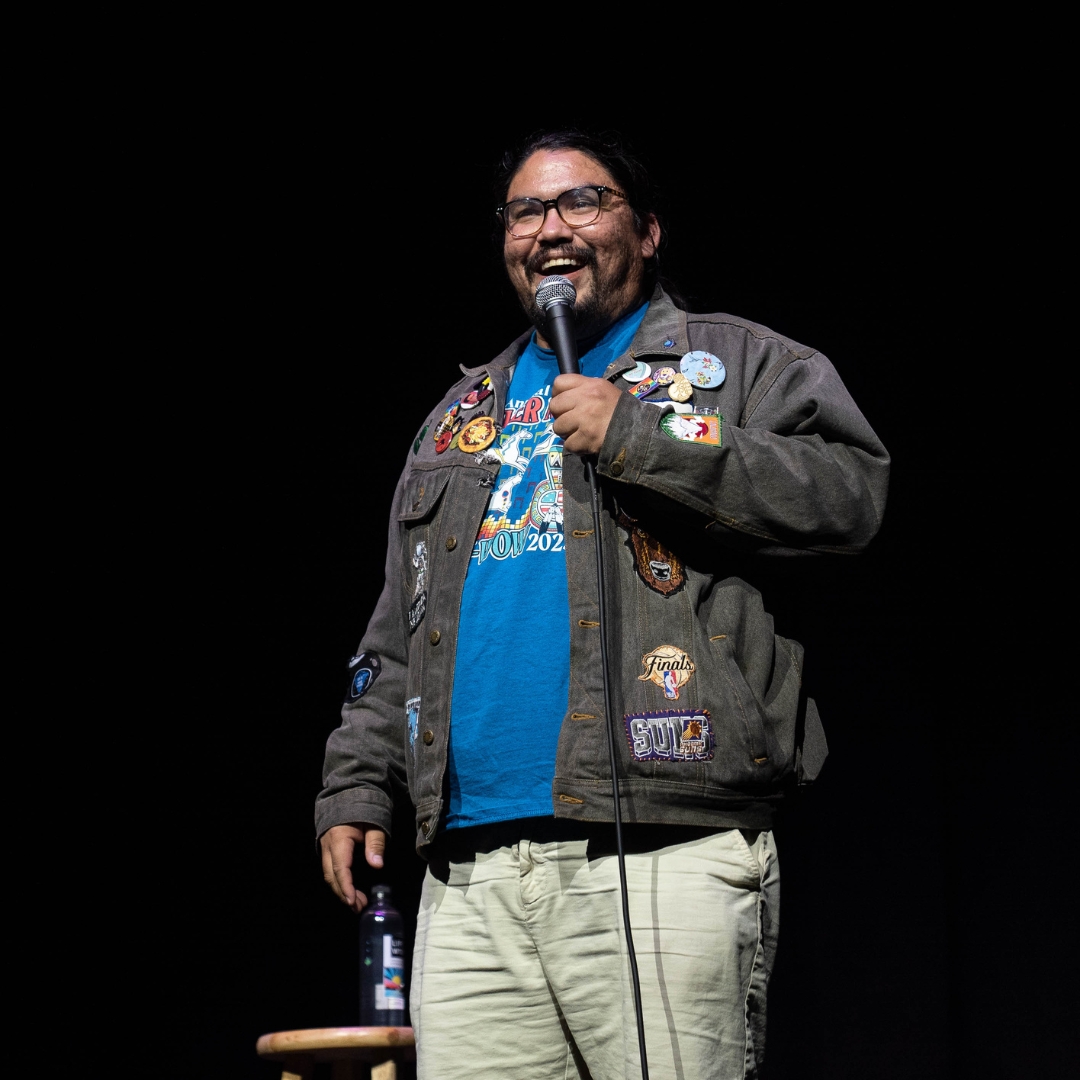 Comedian on stage holding and microphone and smiling.