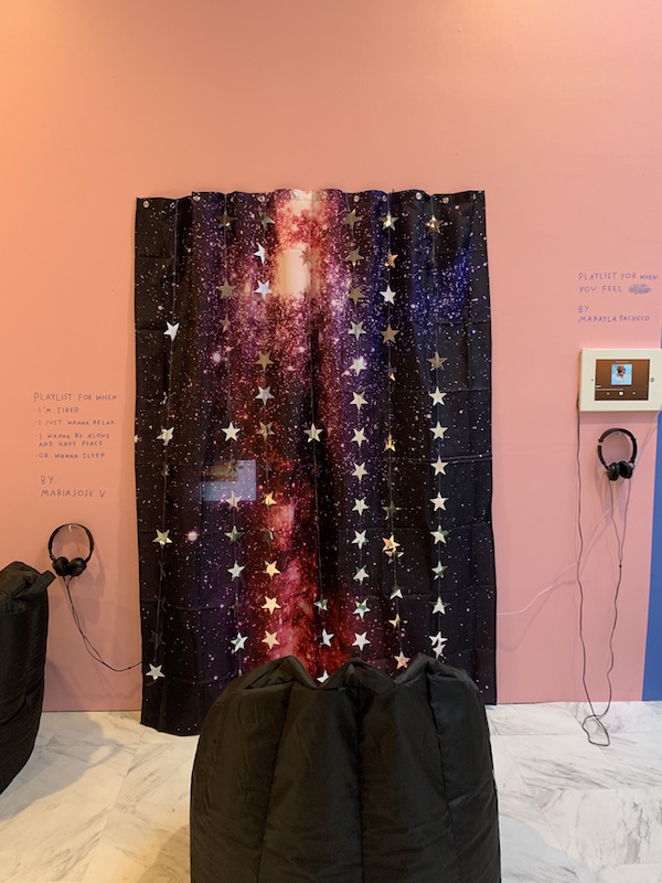 A shower curtain depicting the galaxy hangs on the wall. Text on the wall reads “Playlist for when I’m tired” above a pair of headphones. 