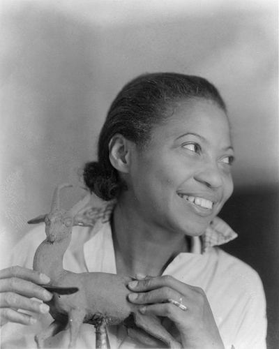 black and white portrait of the artist. Augusta Savage is looking away from the camera, her hands sculpting a figurine. 