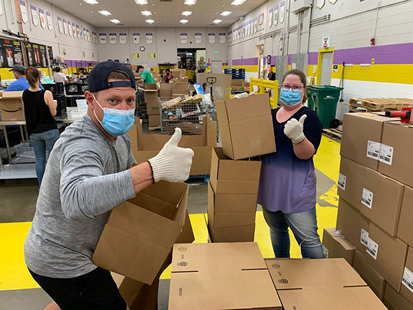 two volunteers wearing masks giving a thumbs up while loading boxes of food donations