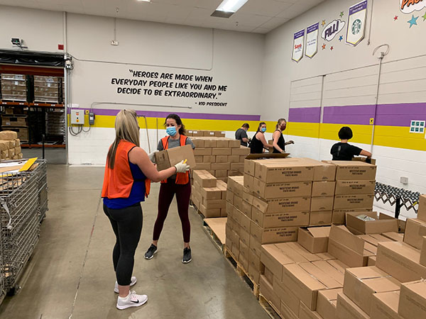 Volunteers in the distribution center loading boxes with a quote on the back wall "Heroes are made when everyday people like you and me decide to be extraordinary." back wall "