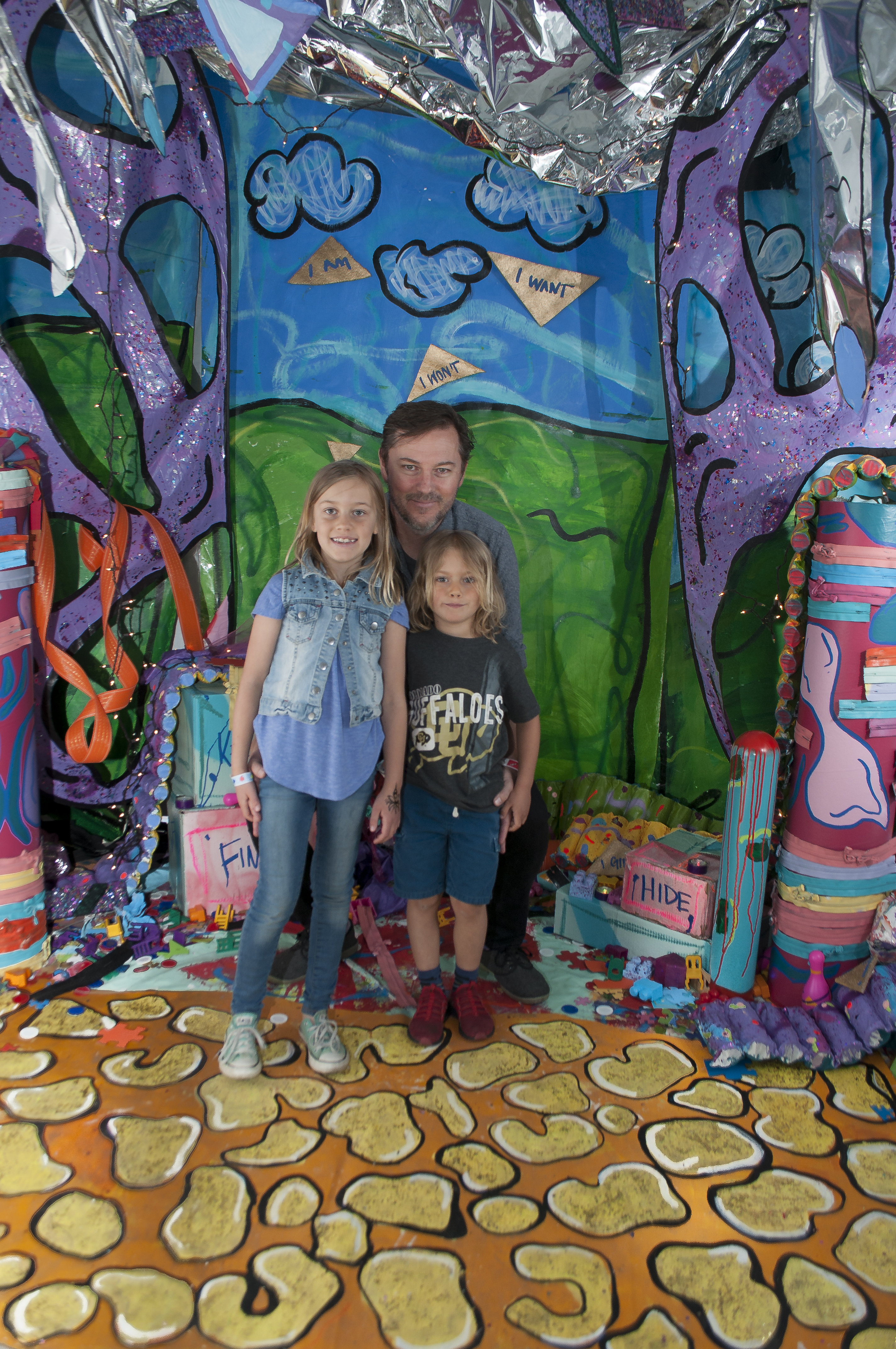 A dad poses with his children in front of a colorful set. 