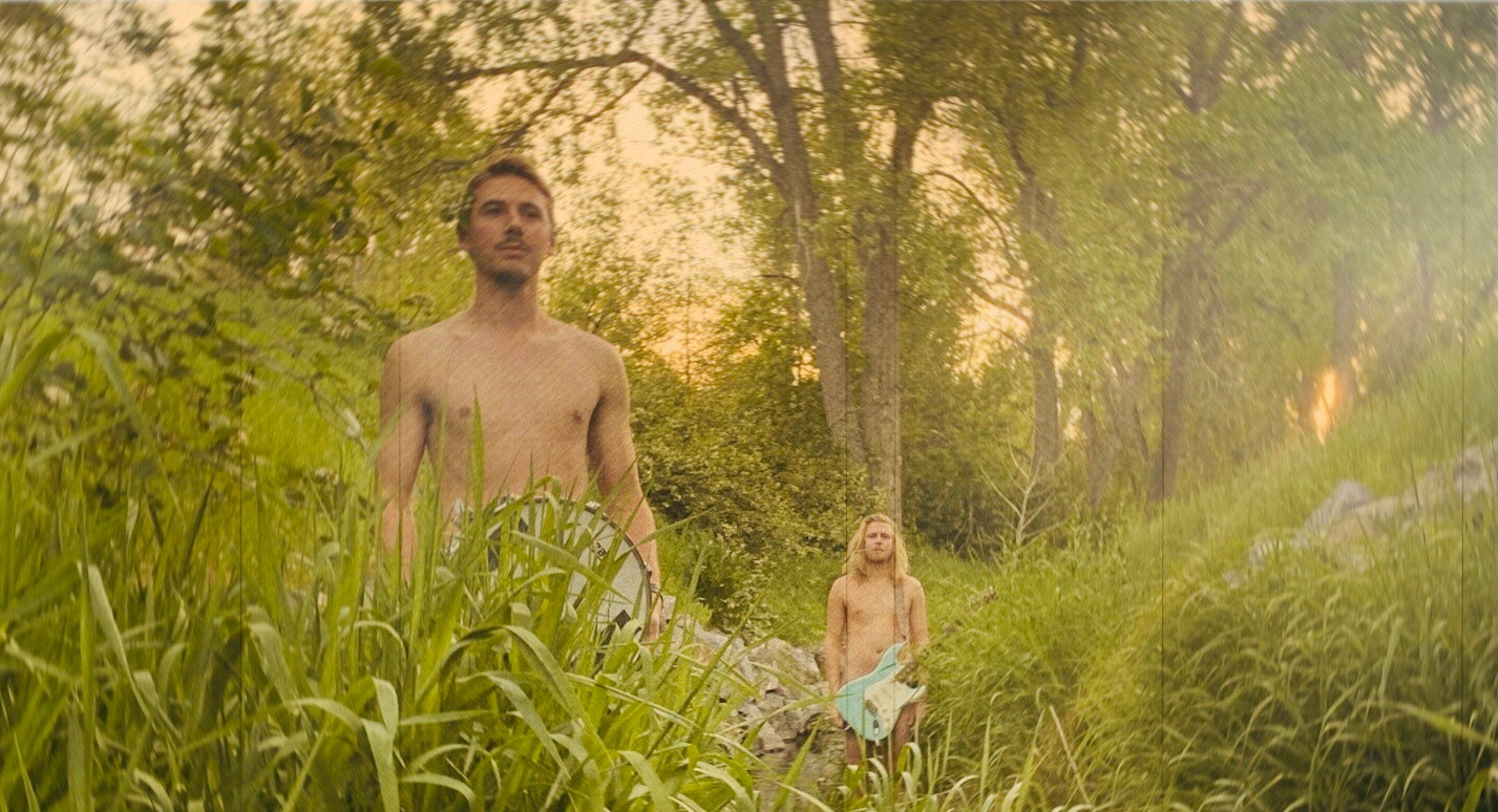Band photo of Fly Amanita standing in tall grass, naked with their instruments in front of them