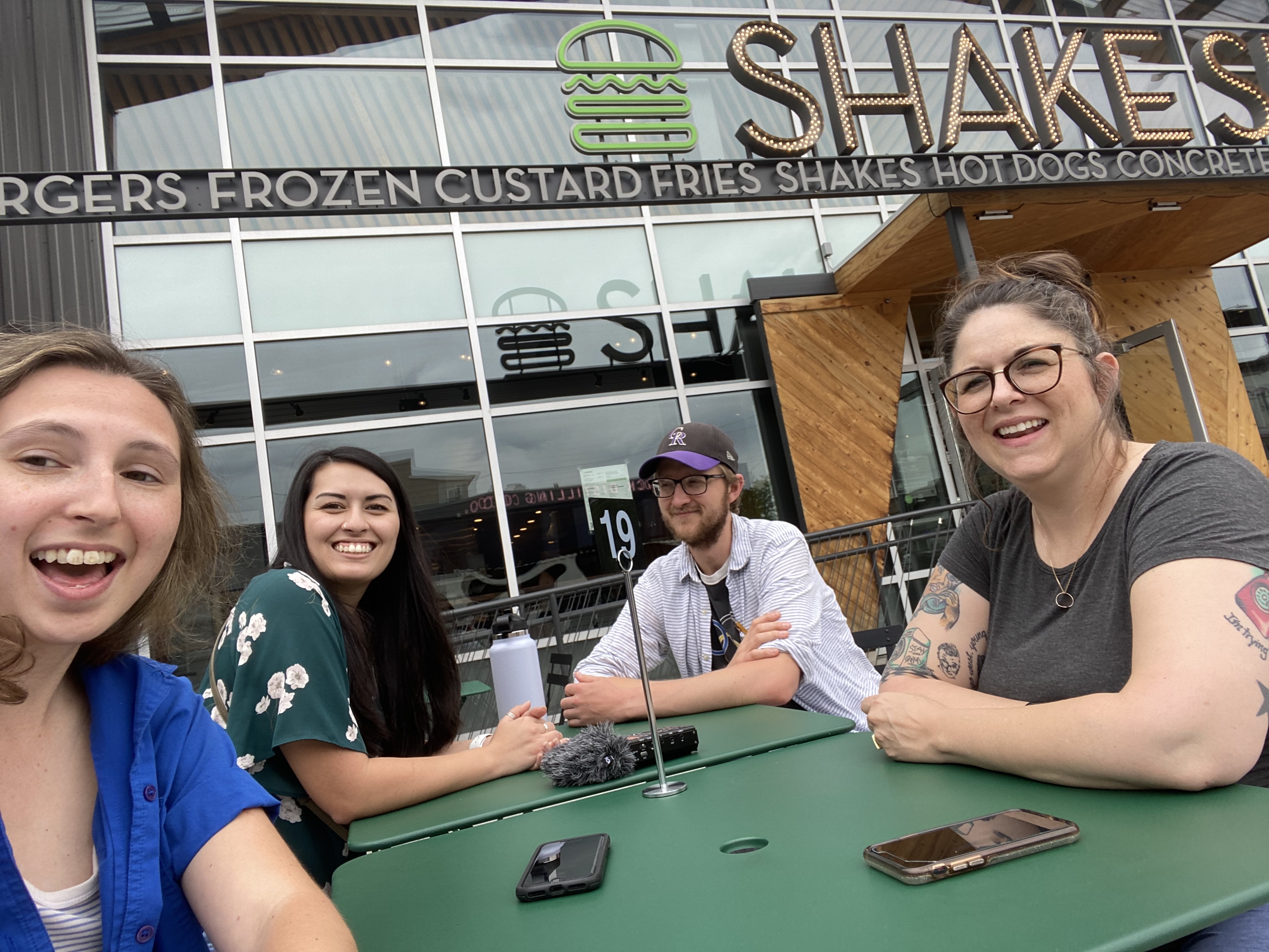 Group photo of the team behind City Cast Denver sitting at a picnic table in front of Shake Shake
