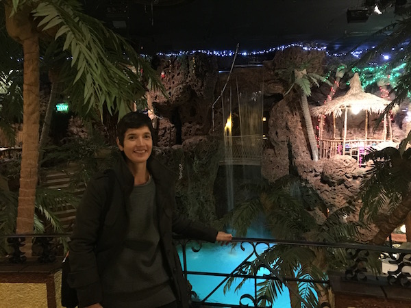 Sierra posing at Casa Bonita. There is a blue pool behind her and fake palm trees. 
