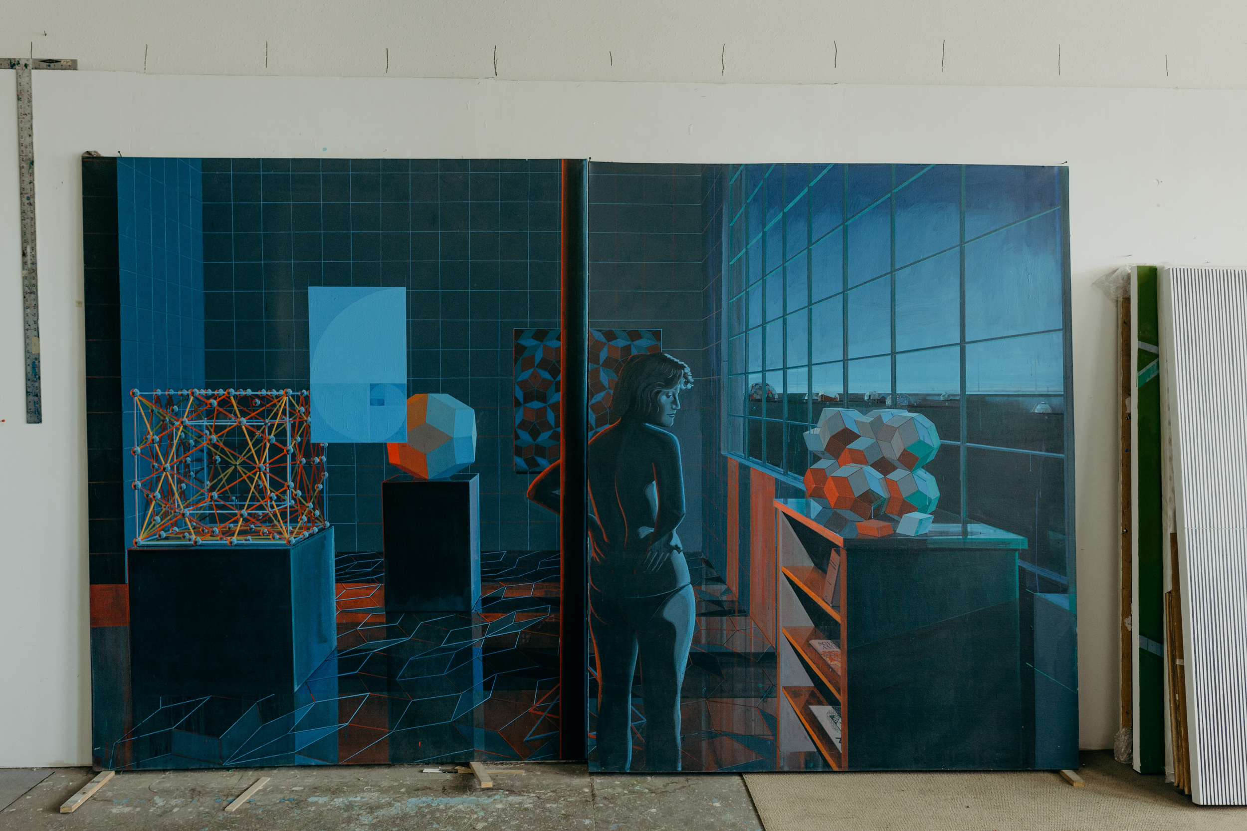 A large painting is leaning against a wall. It depcits a topless woman at night in an indoor space. She is looking at a geometrical model on a pedastel. 