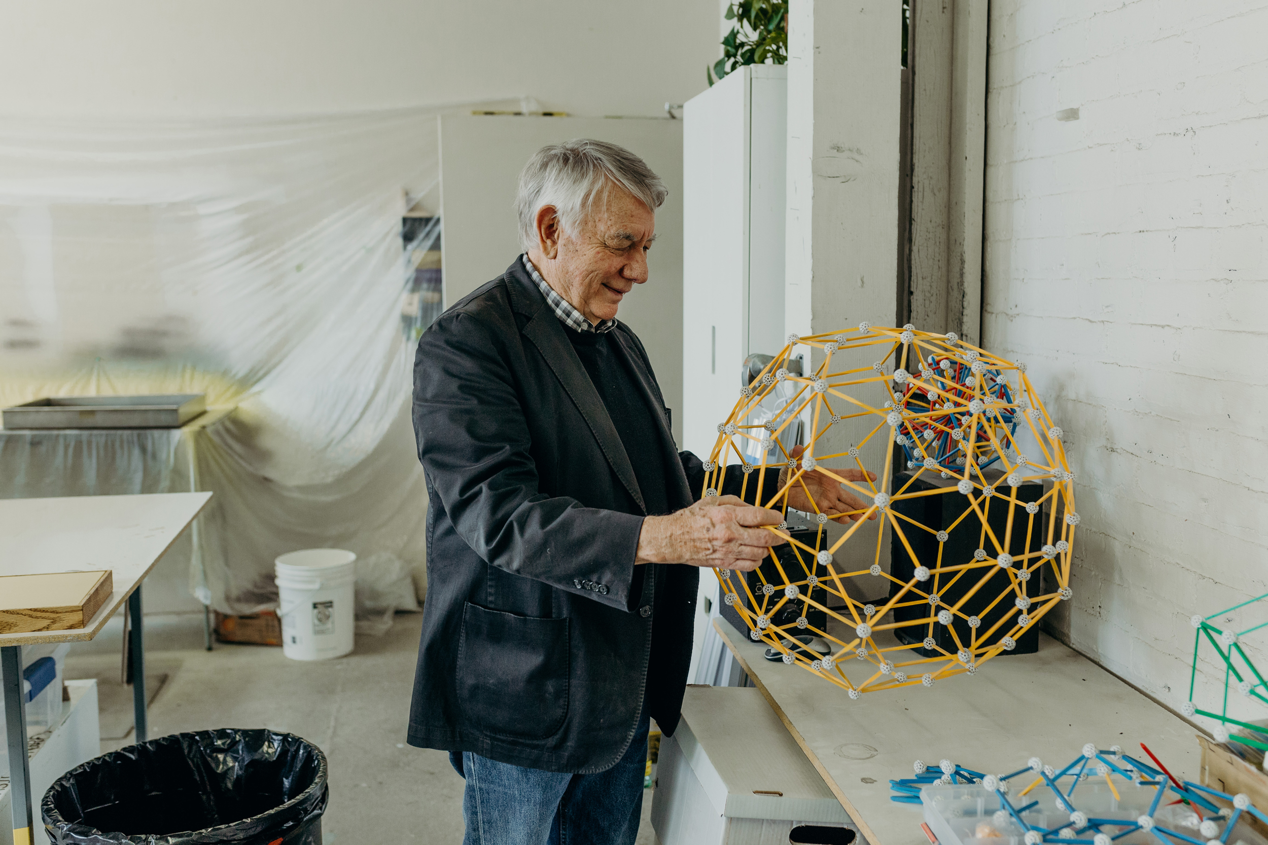 Clark Richert is holding a large yellow geometrical model in an indoor space. 