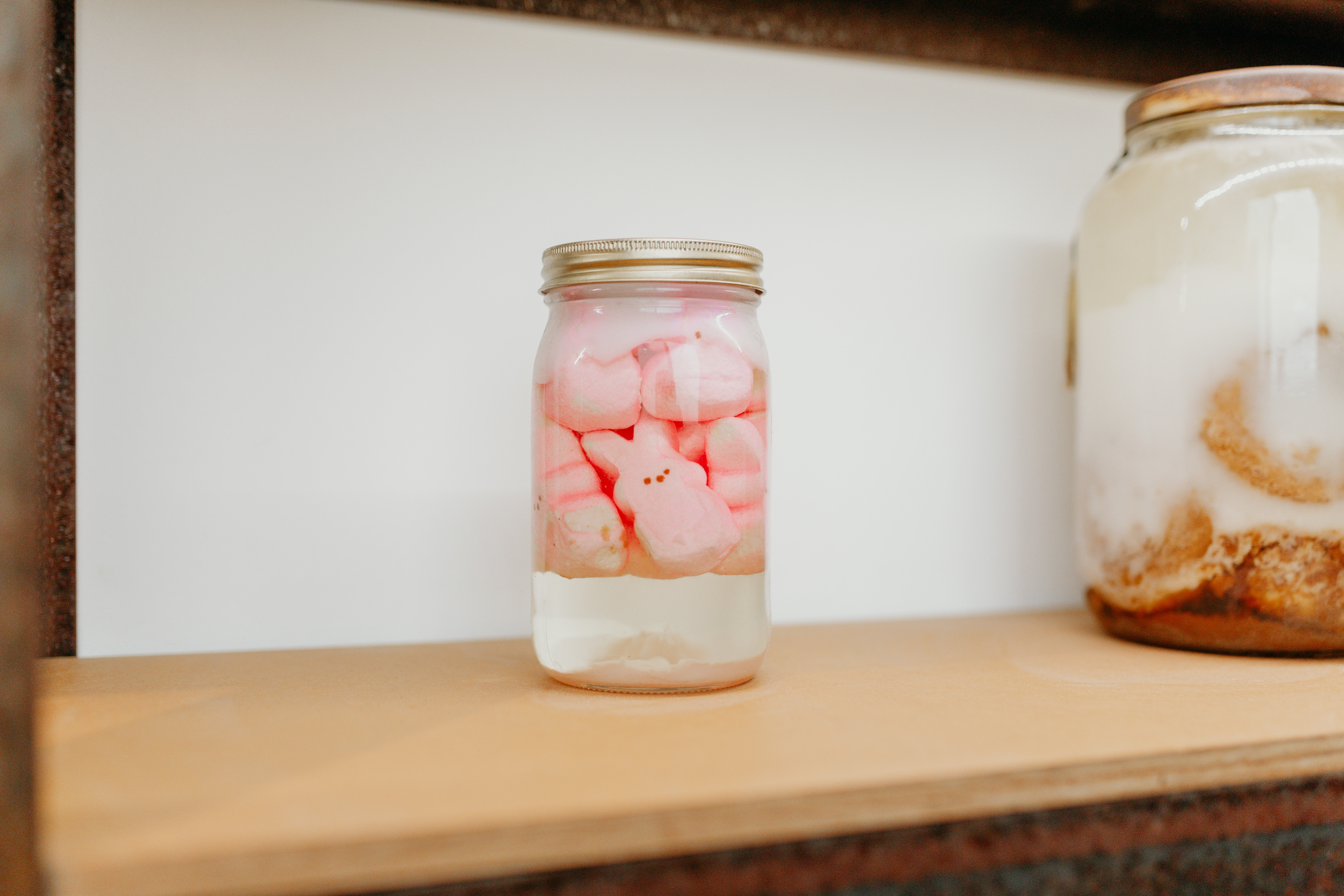 A mason jar rests on a wooden shelf. Inside are floating pink bunny candies commonly sold during easter. 