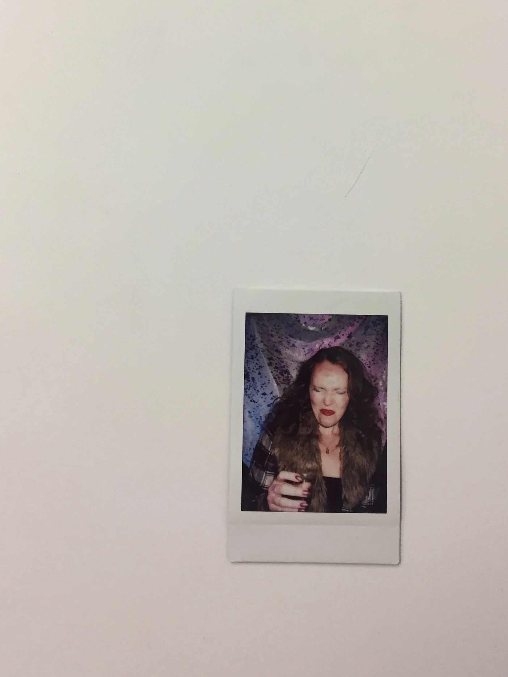 A polaroid of a young woman cringing after taking a shot of liquor. 