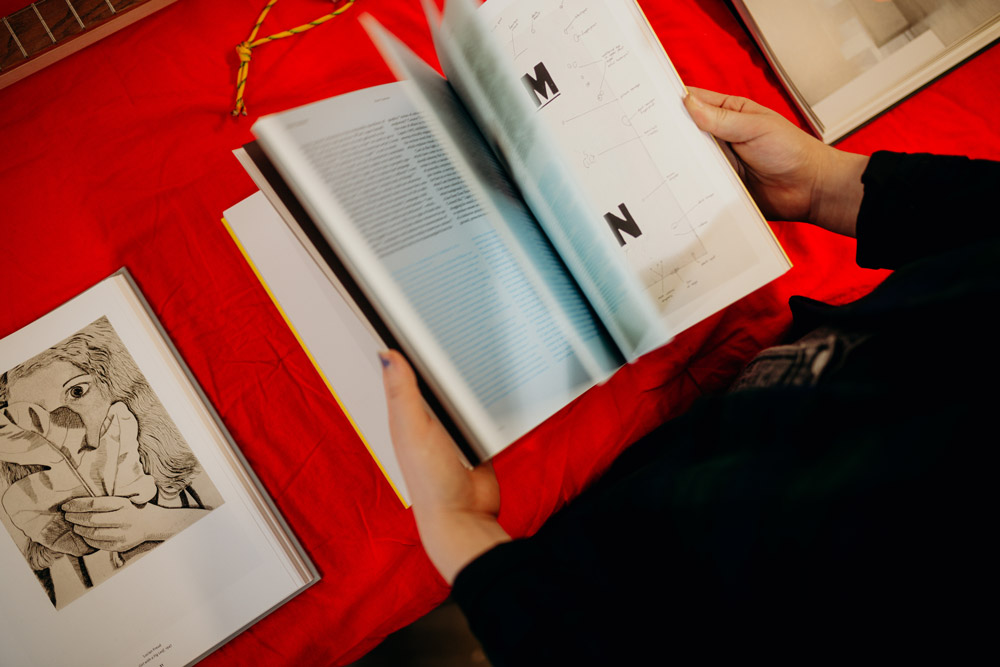 Two hands flip through a book against a red backdrop. The pages are blurred in movement. 