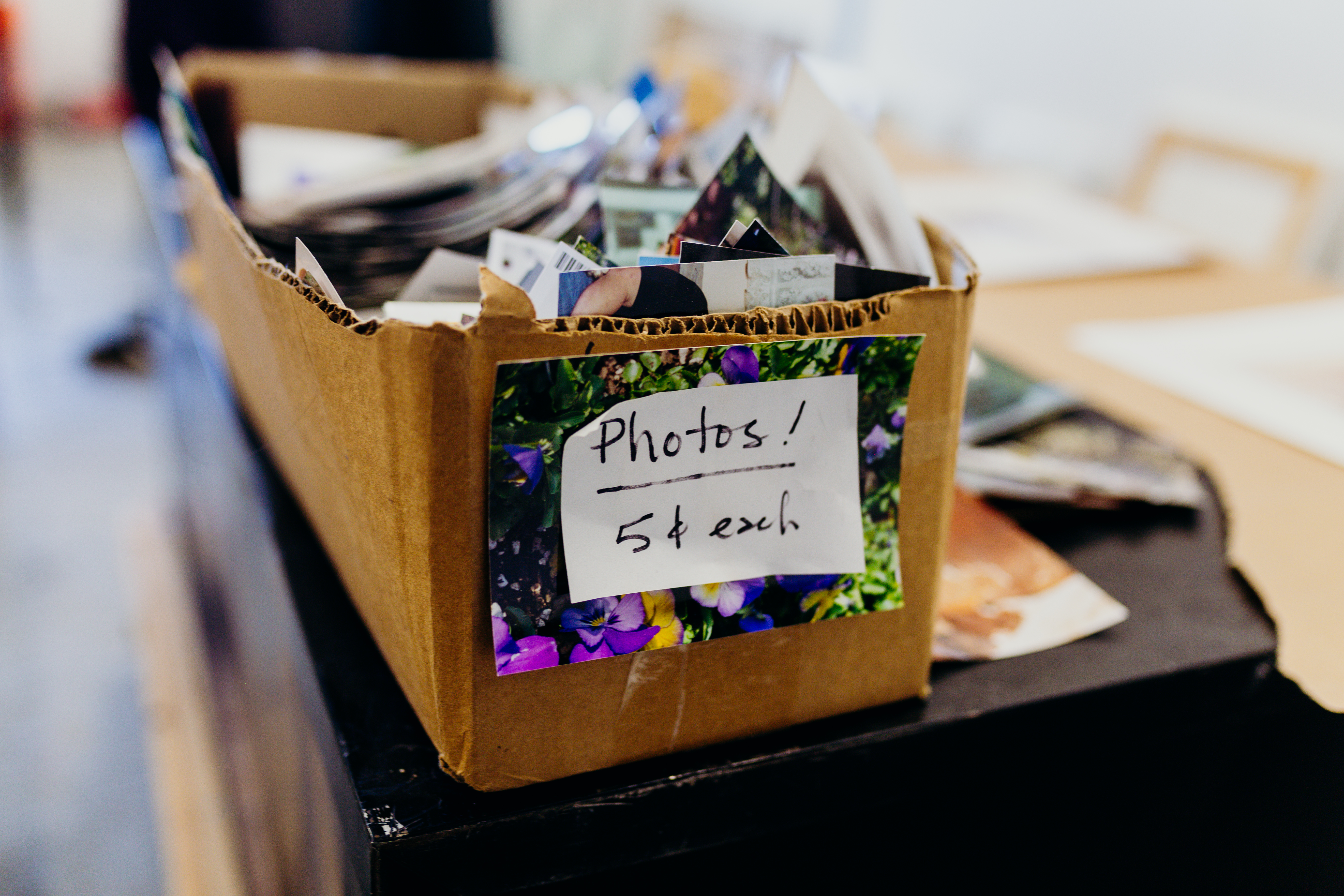 A cardboard box filled with many photographs. There is a piece of paper taped to the word that reads: Photos! 5 cents each