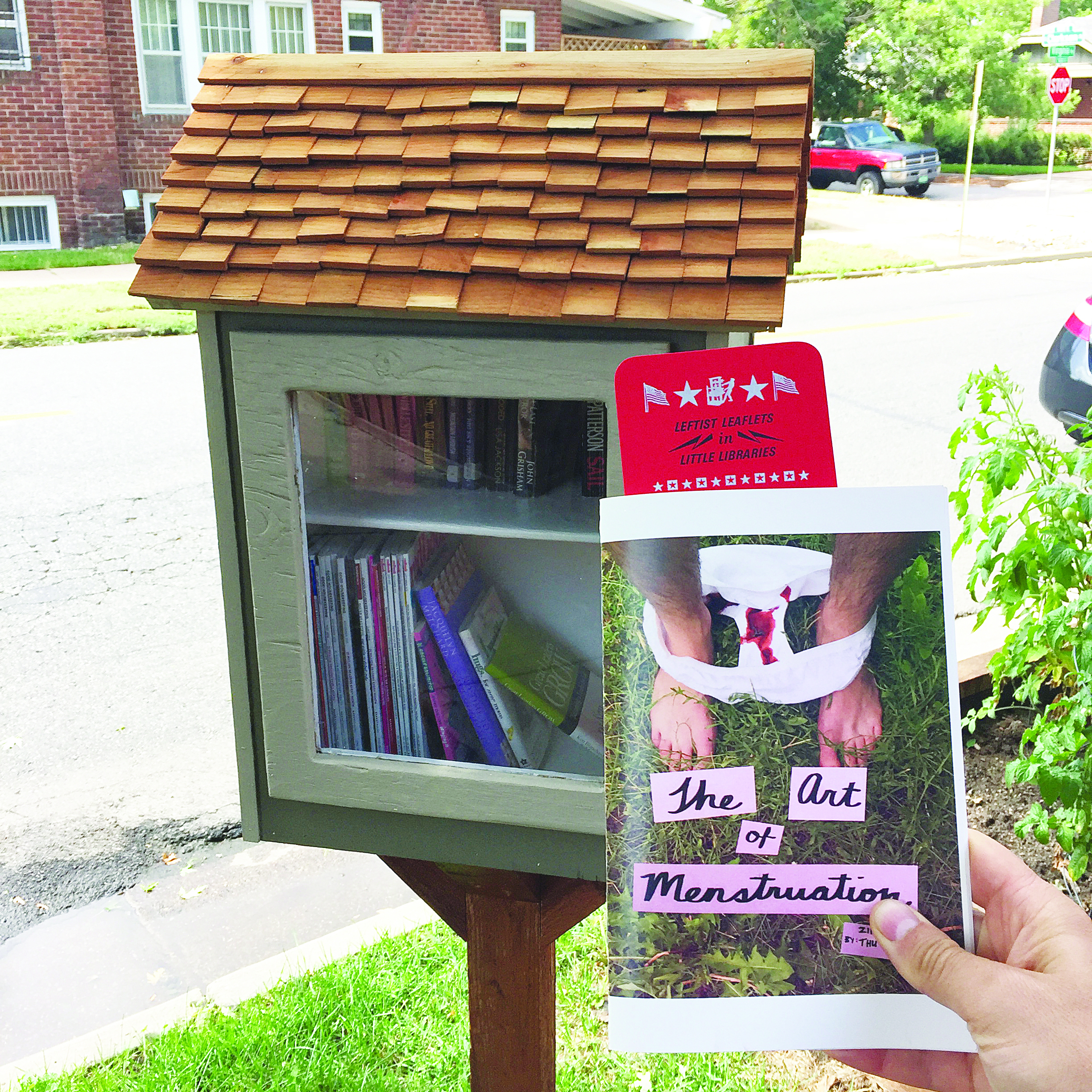 A small library in the shape of a house with booklets inside. There is a hand holding a zine that says "The art of menstruation."