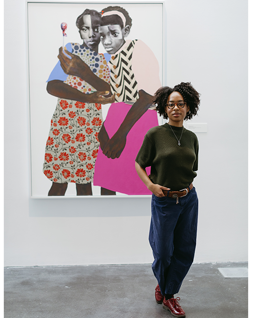Portrait of Nadiya Jackson standing in front of, The unseen, large mixed media canvases by artist Deborah Roberts