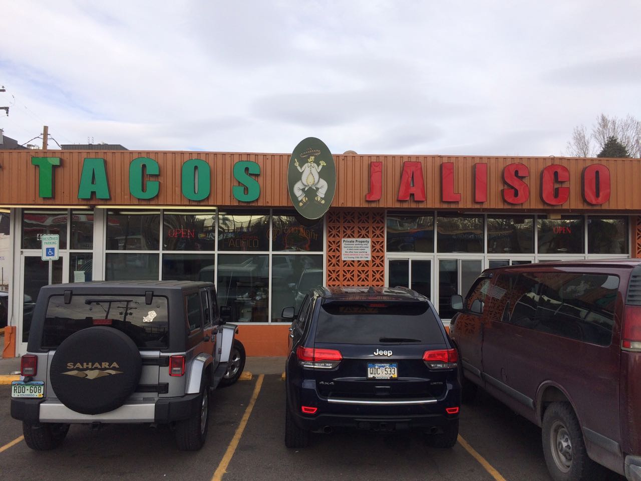 A restaurant named Tacos Jalisco with cards in the parking lot. 
