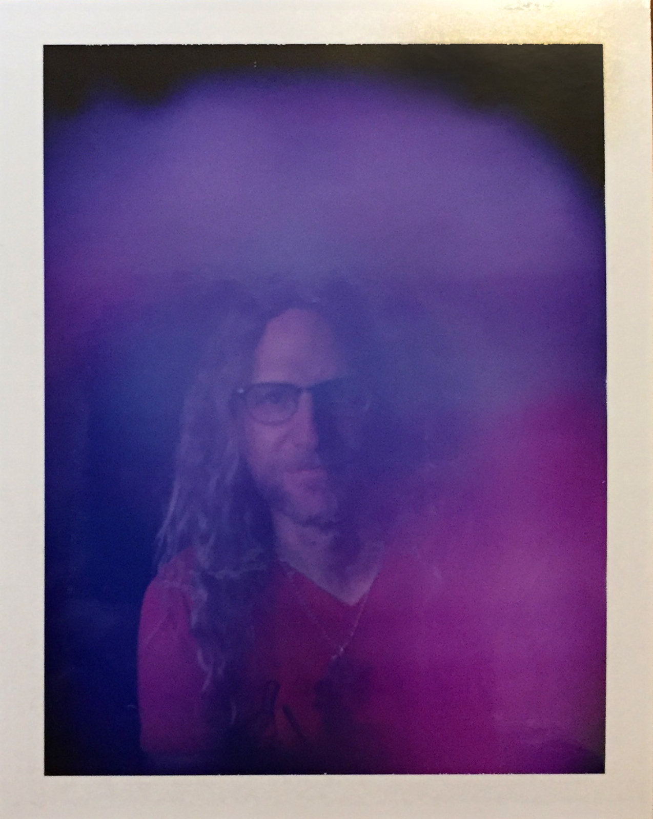 A polaroid photo of Peter, surrounded by a purple aura. He is wearing glasses and smiling softly. 