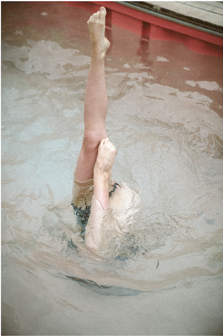 Two legs emerge vertically from a pool of water as part of a water dance routine.