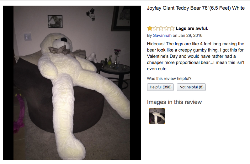A human sized white teddy bear is propped against a couch. 