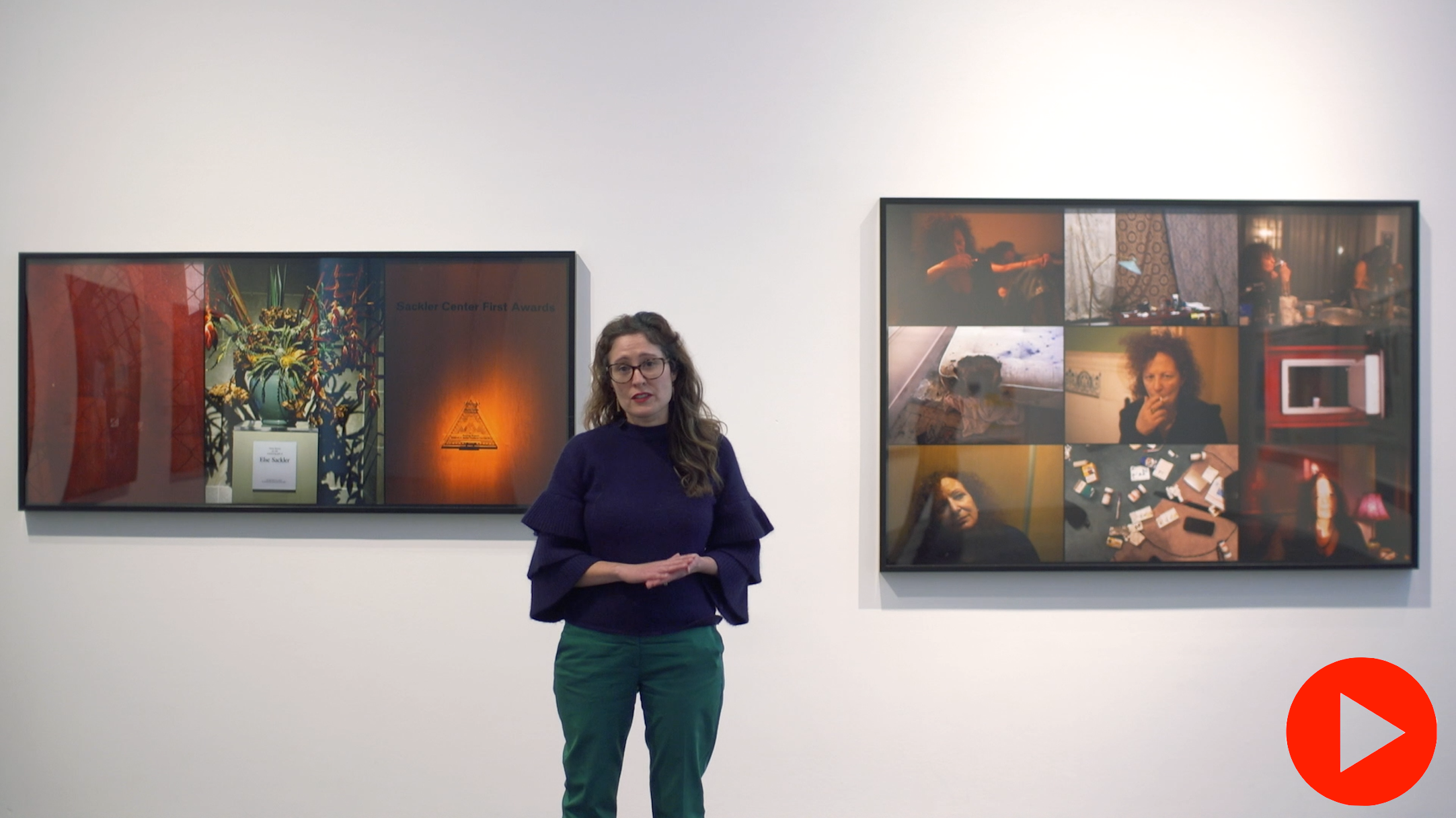 Image of Miranda Lash standing in a gallery wearing a navy blue sweater with forest green pants. She stand in between two rectangular artworks by artist Nan Goldin. 