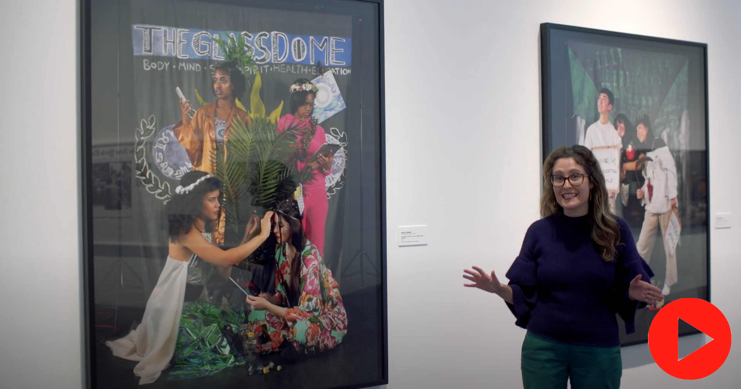 [Image description: Miranda Lash stands in front of Adelita Husni-Bey's work in the gallery. A red play button is in the bottom right corner.]
