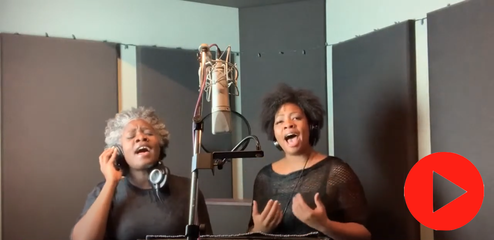 Two women (Spirit of Grace) in black shirts sing in front of a studio microphone in a room with soundproof padding on the walls.