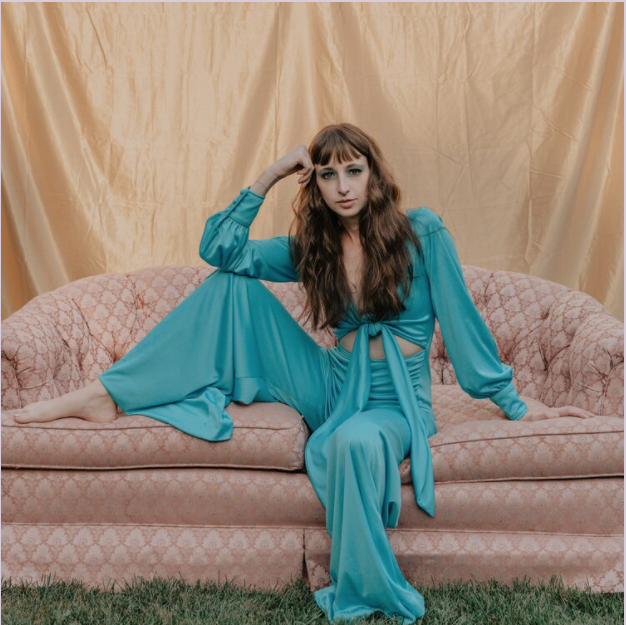 Outdoor portrait of Steffie Collins sitting on a couch in a green flowing jumpsuit