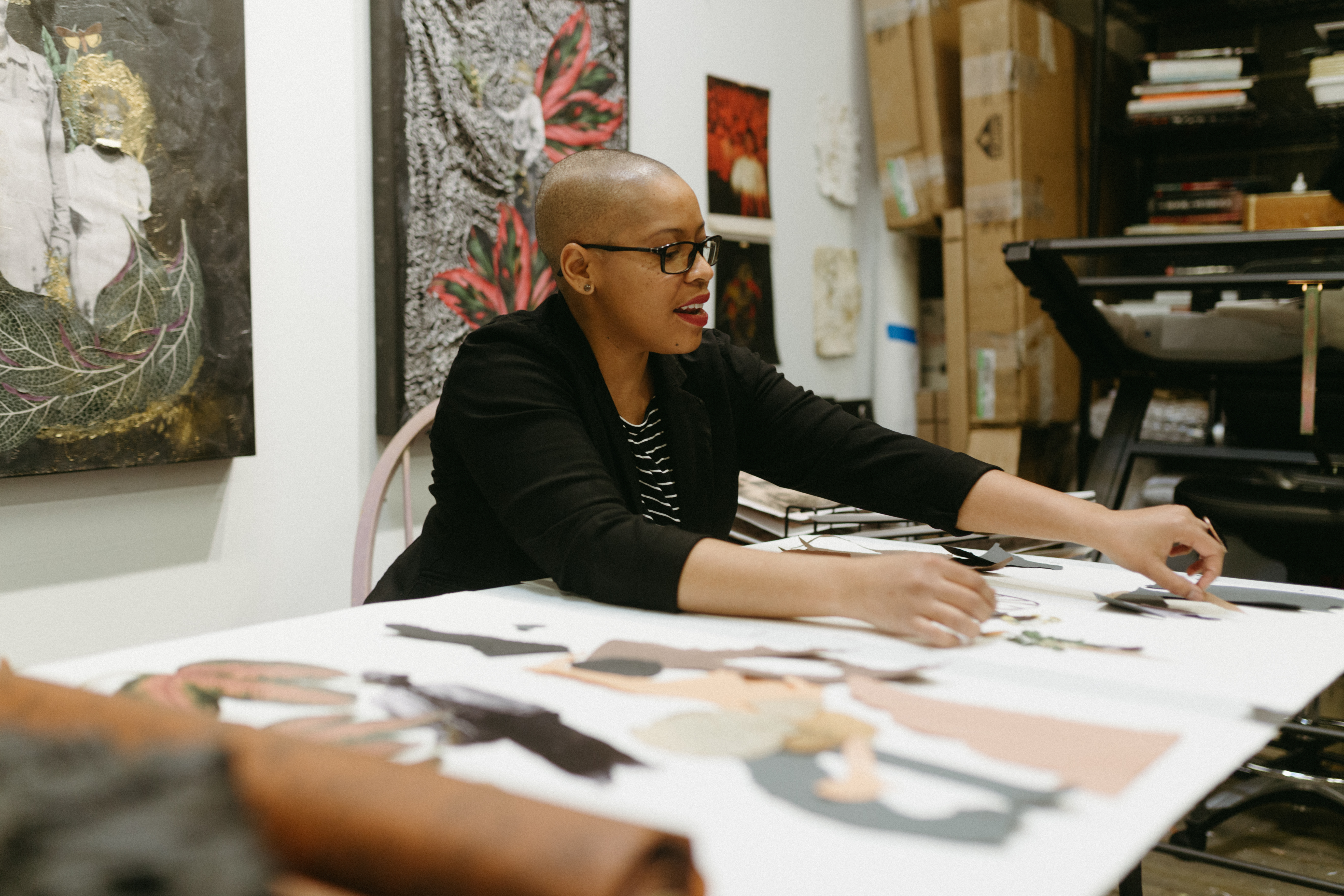 Anthony working on a collage in her studio. She is wearing a black blazer and is smiling. 