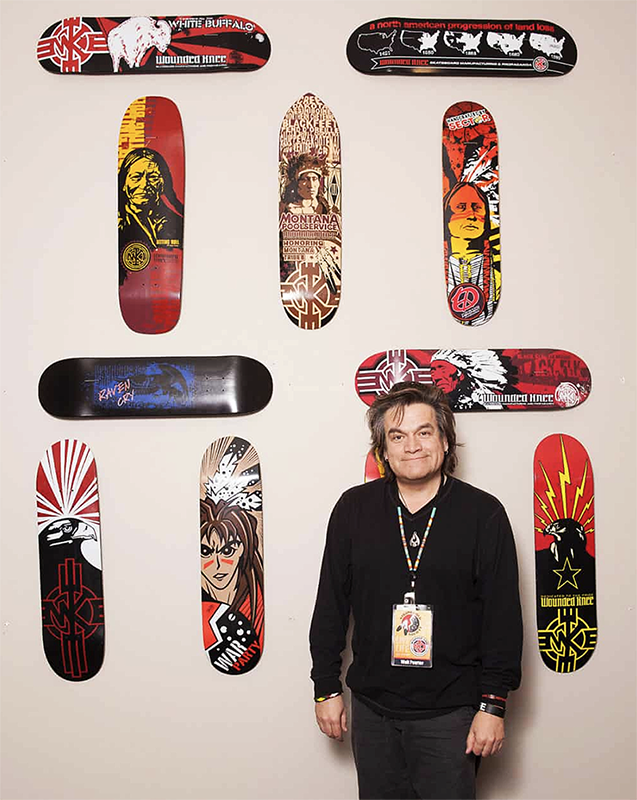 Photo of artist, Walt Pourier in from of skateboard decks designed by the artist