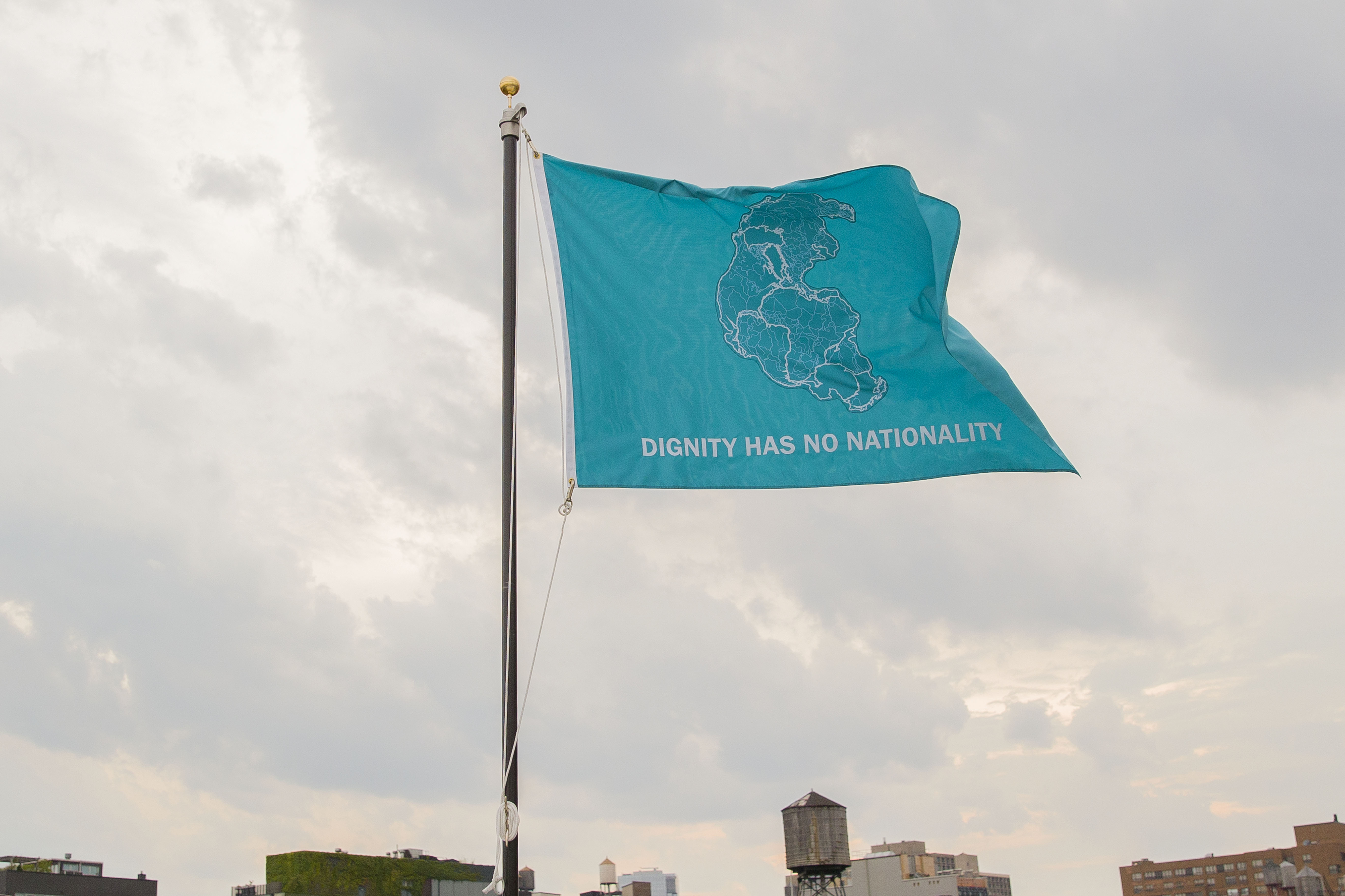 Light blue flag flying that says "dignity has no nationality" in all caps with a drawing of Pangea in the center. 