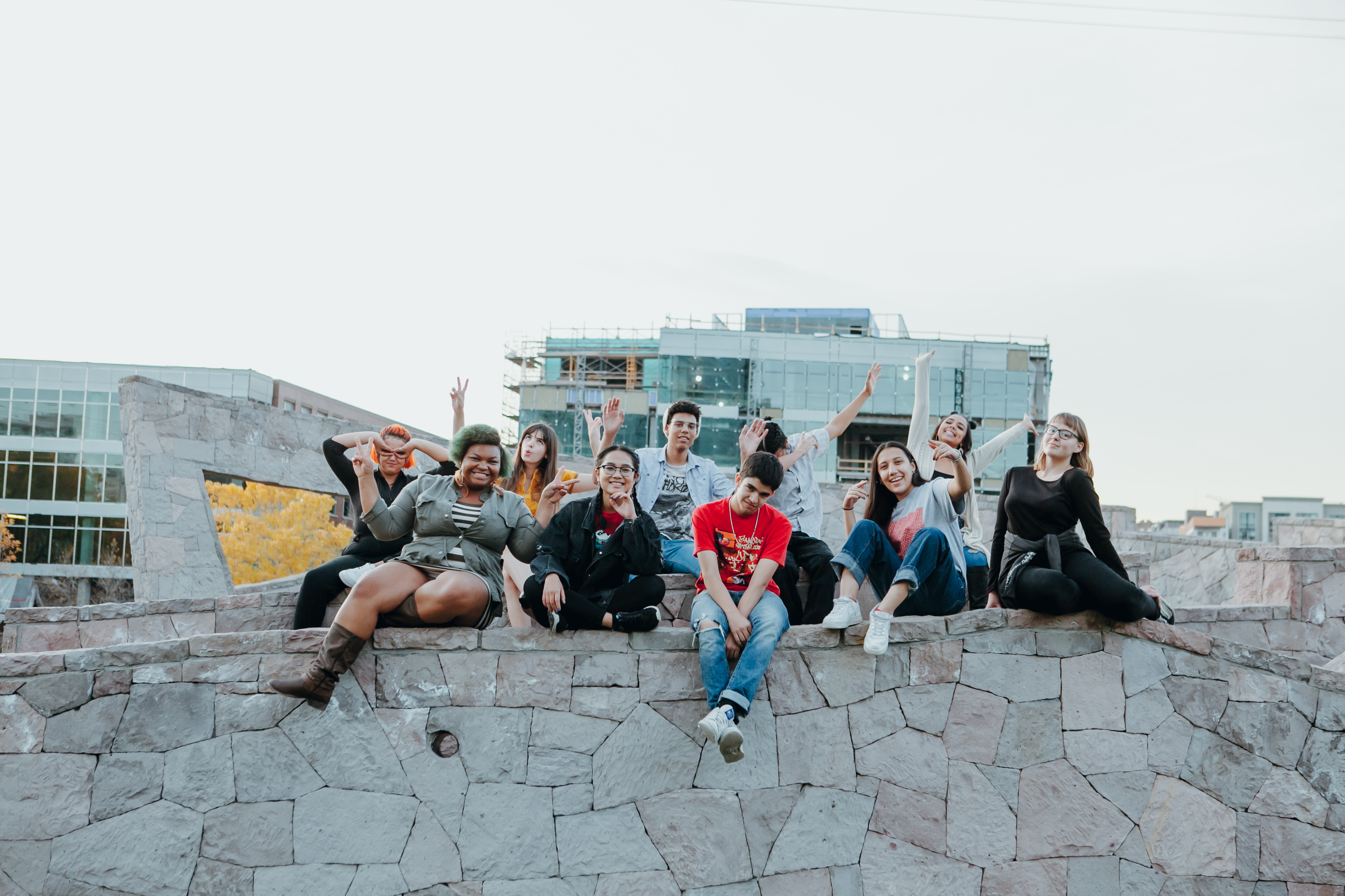 A group of diverse young adults pose for a photograph seated on a stone ledge. 