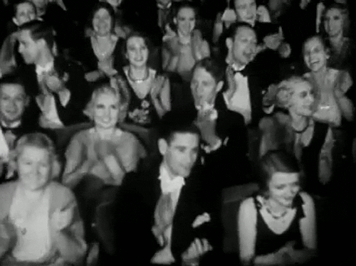 A black and white animated picture of an old-timey audience in suits and dresses clapping.