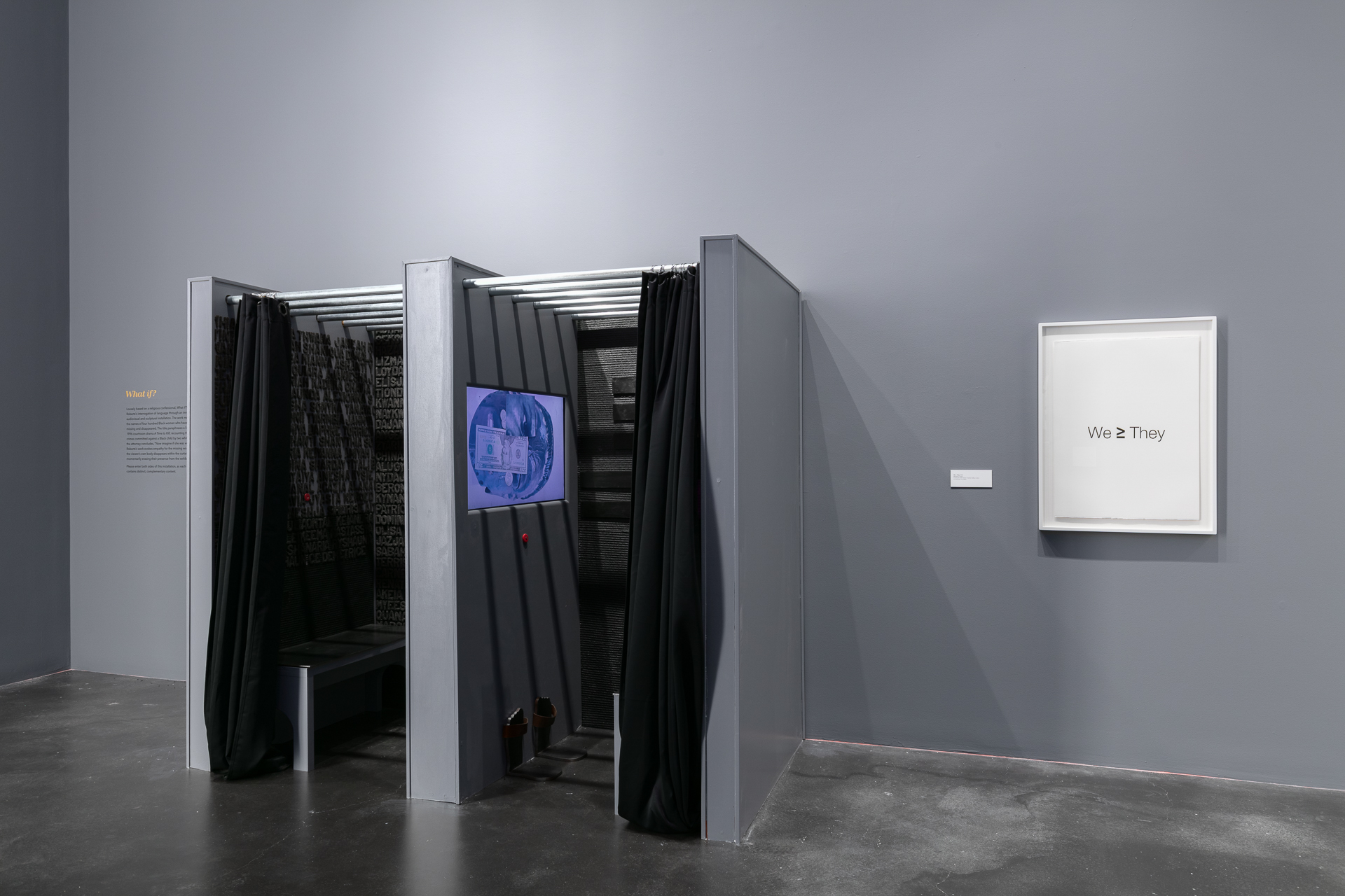 [Image description: A photograph taken in the museum of the work "What if?" by Deborah Roberts. It looks almost like a confessional booth with two curtained sides. On the walls, felt letters can be seen spelling out names of women. A video screen is visible on the wall in one side.]
