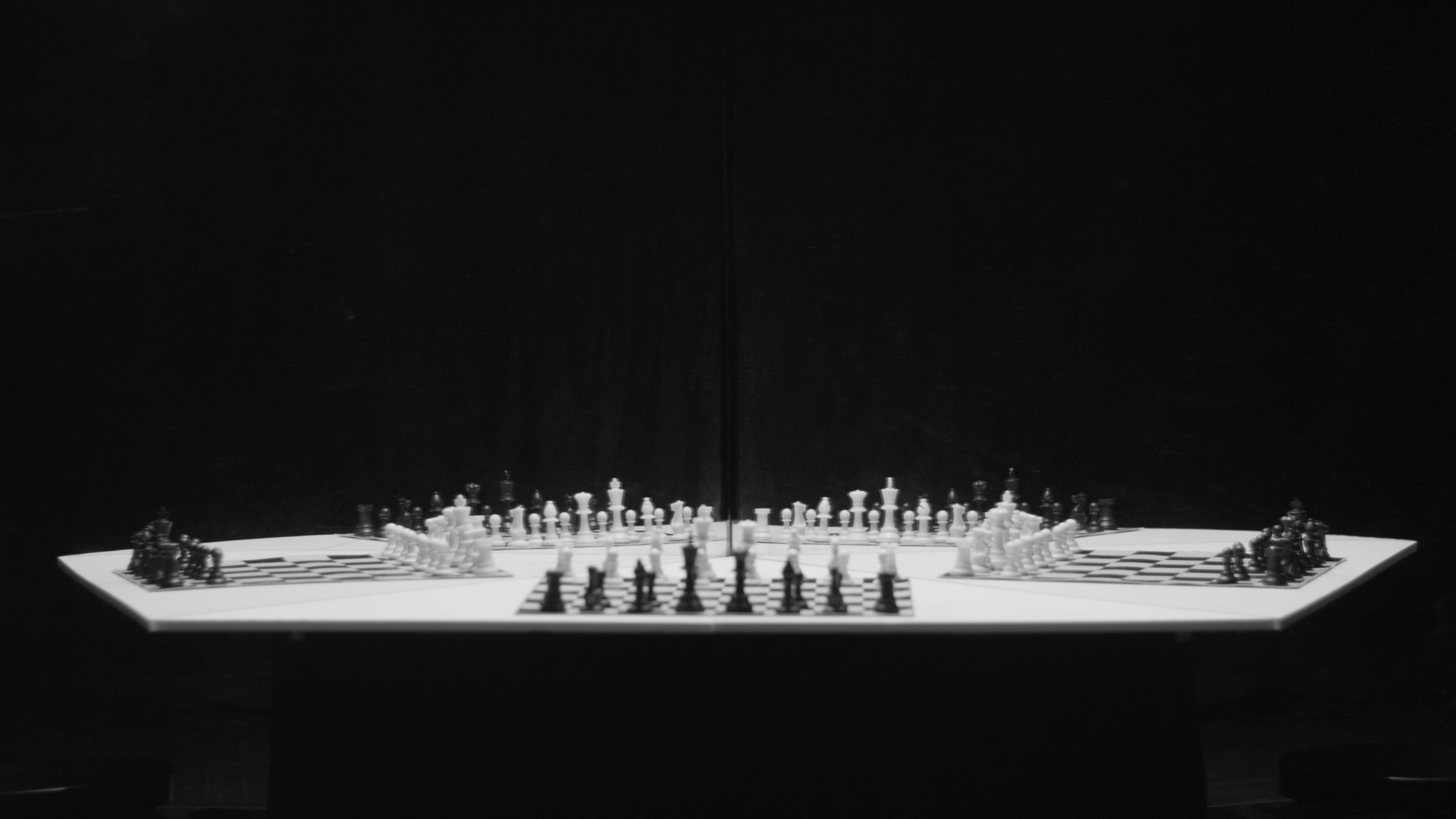 [Image description: A black and white still from the film Chess by Lorna Simpson. In the image, a pentagon-shaped chess board is lined with chess pieces.]