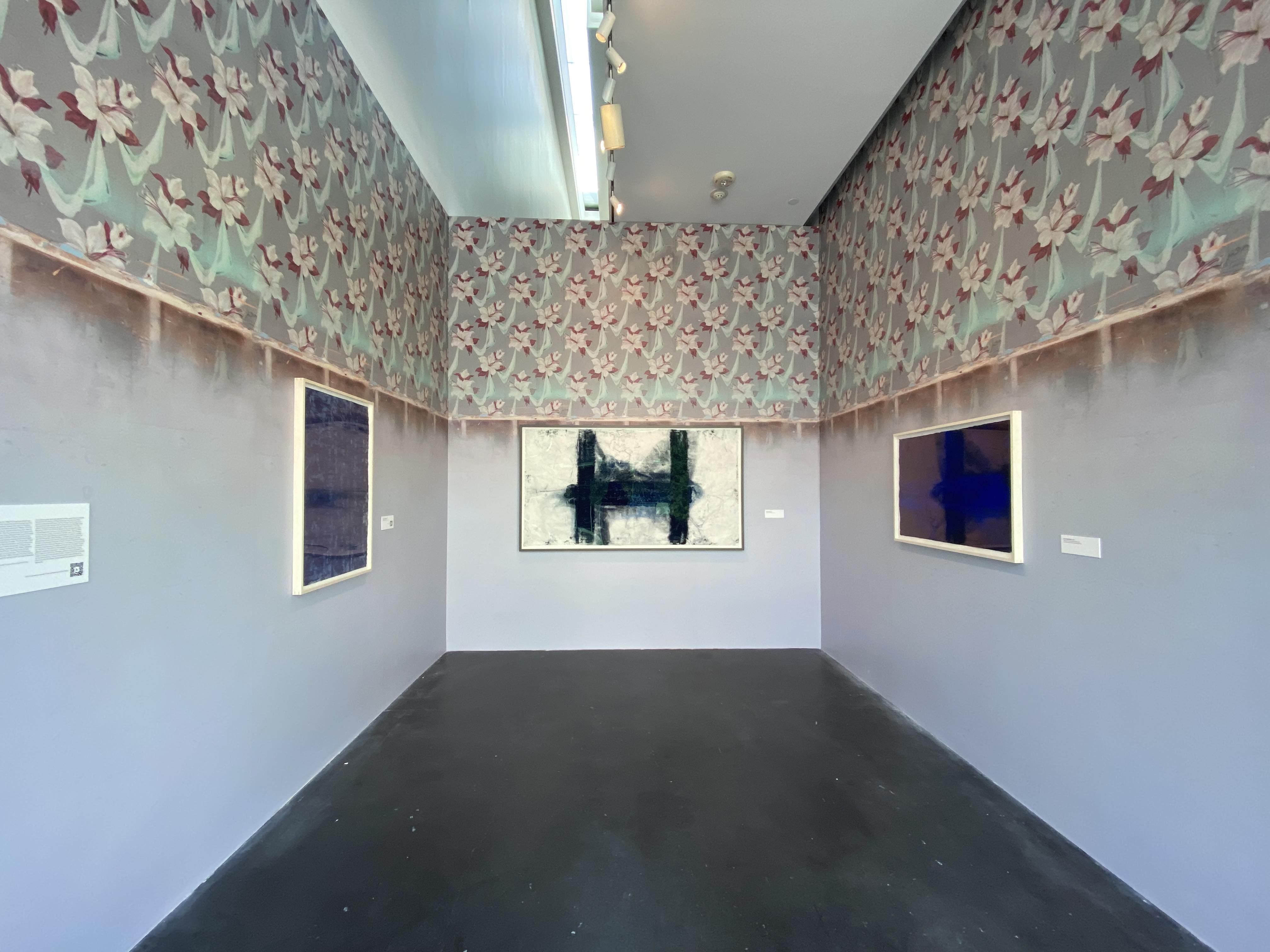 [Image description: A photograph of a small gallery in MCA Denver. All three walls are lined with weathered wallpaper with white flowers and light teal cloth between them. On the walls are three paintings by Jason Moran.]