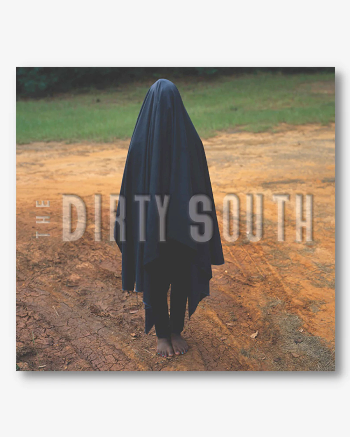 Catalogue with an image of a figure standing barefoot in red dirt, covered in a long black sheet-like material on it. Text on the catalogue reads, "The Dirty South". 
