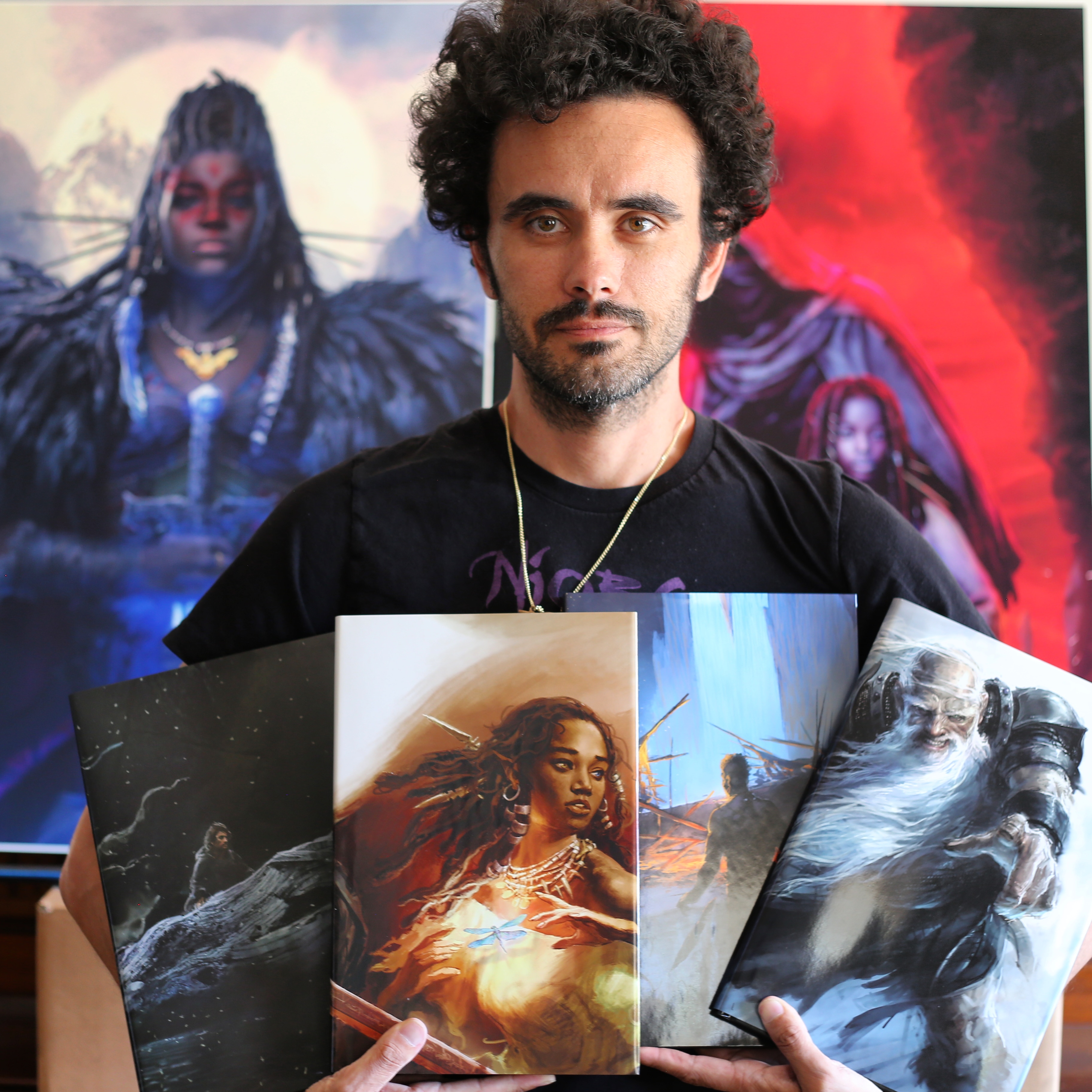 Photo of Sebastian Jones holding four of his books. In the background are large posters of his character Niobe