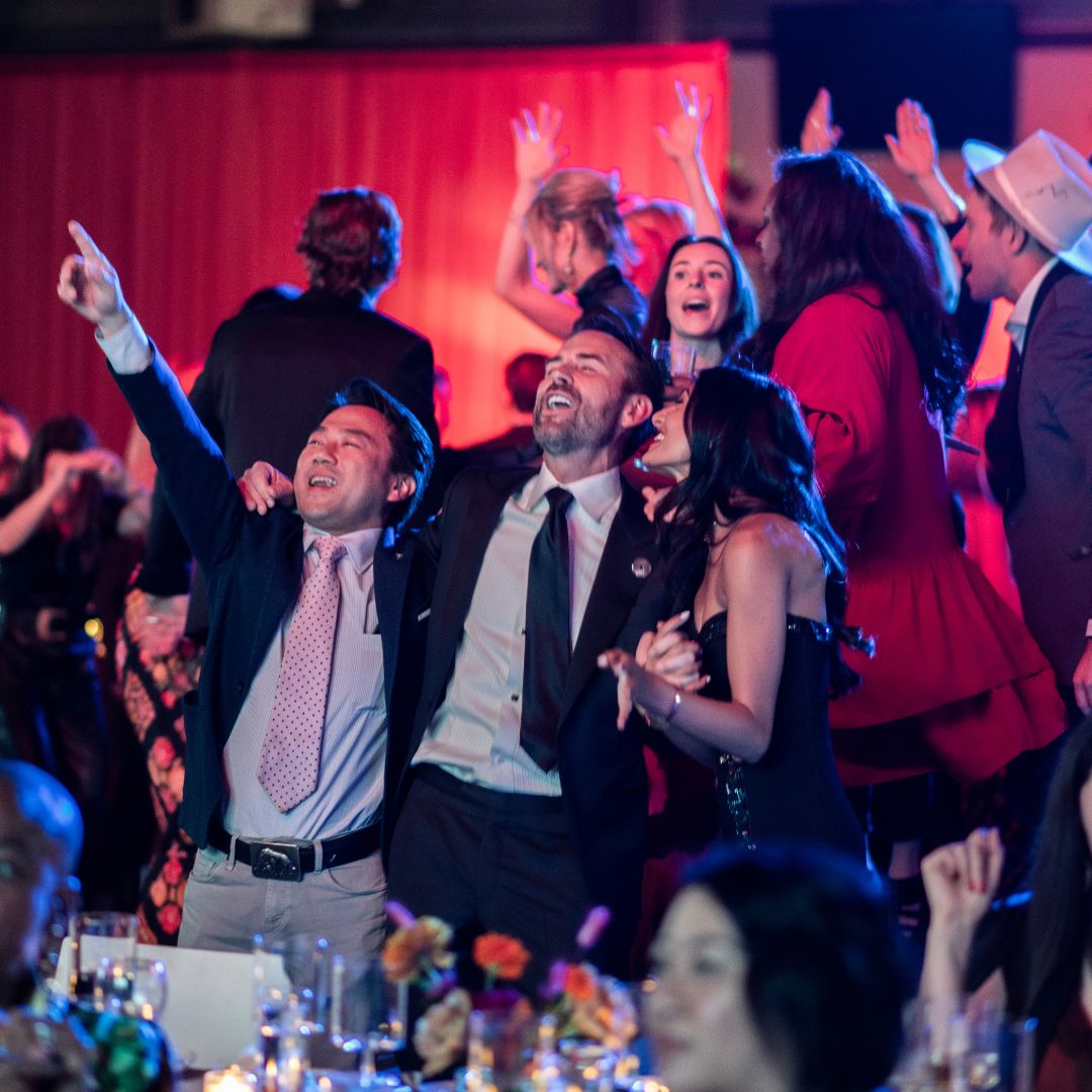People at a gala with their hands around one another, looking like they are singing a song together. 