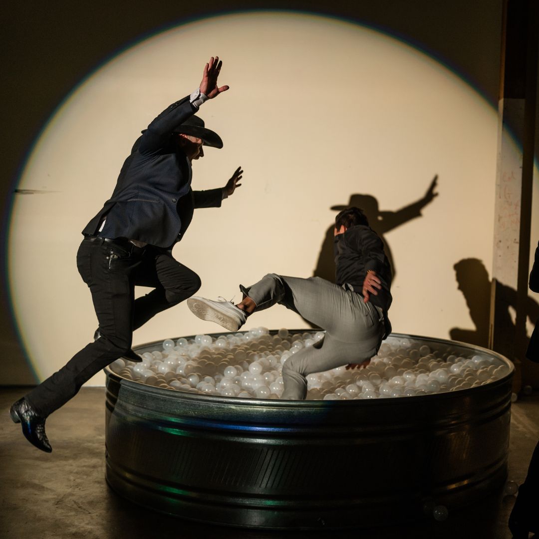 People wearing cowboy hats jumping into a small ball pit.