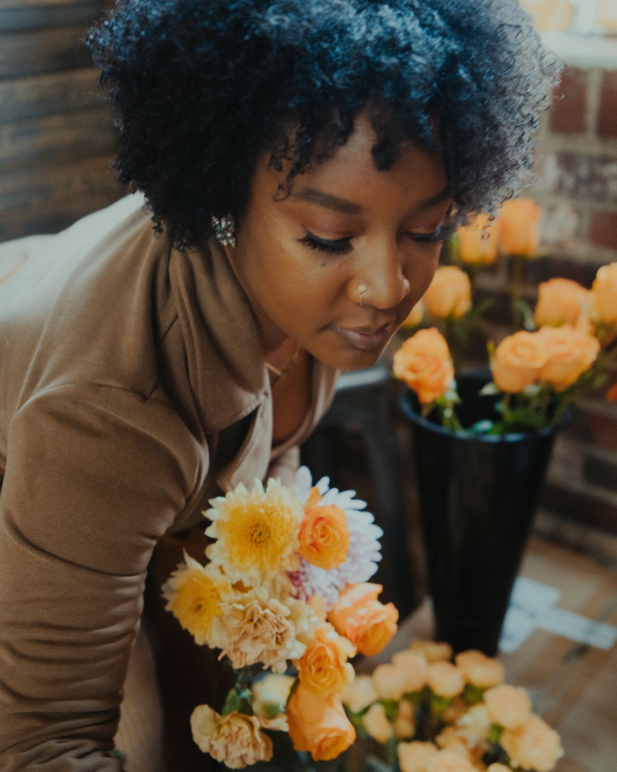 Portrait of Breigh Jones-Coplin looking down at bouquets of orange flowers.