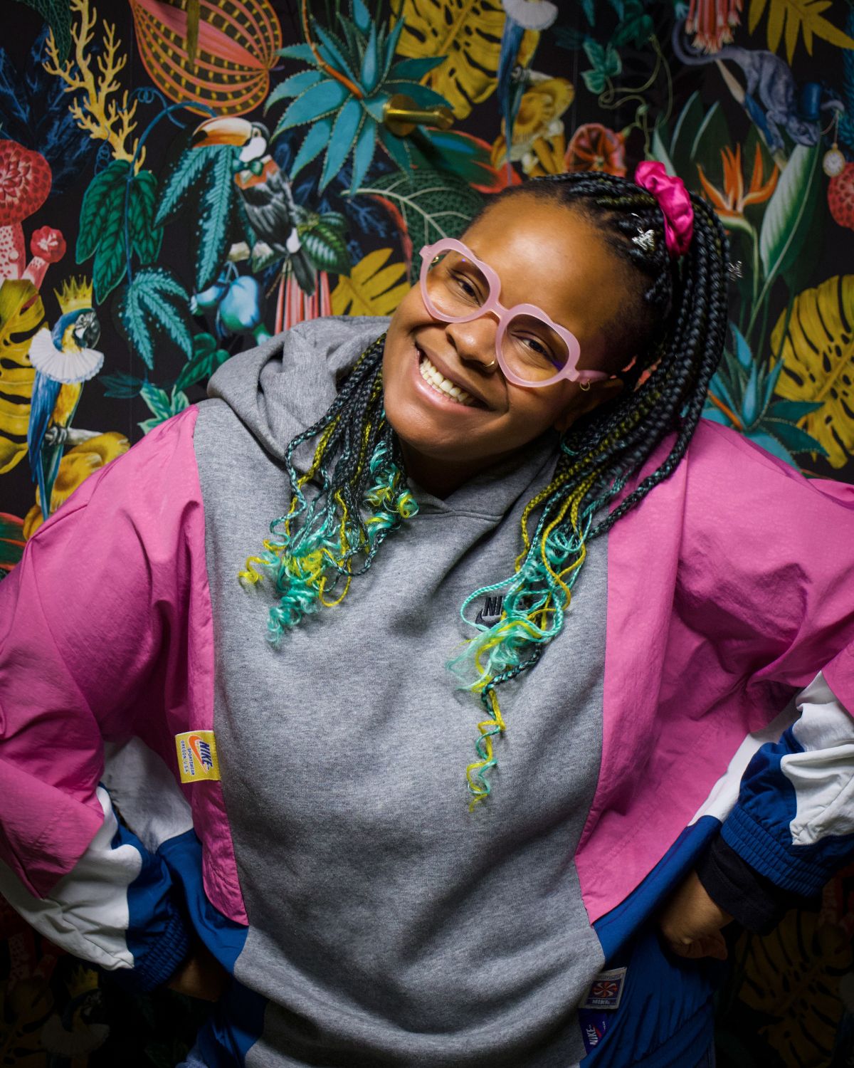 Portrait of Shanel Hughes posing with her hands on her hips in front of colorful wallpaper.