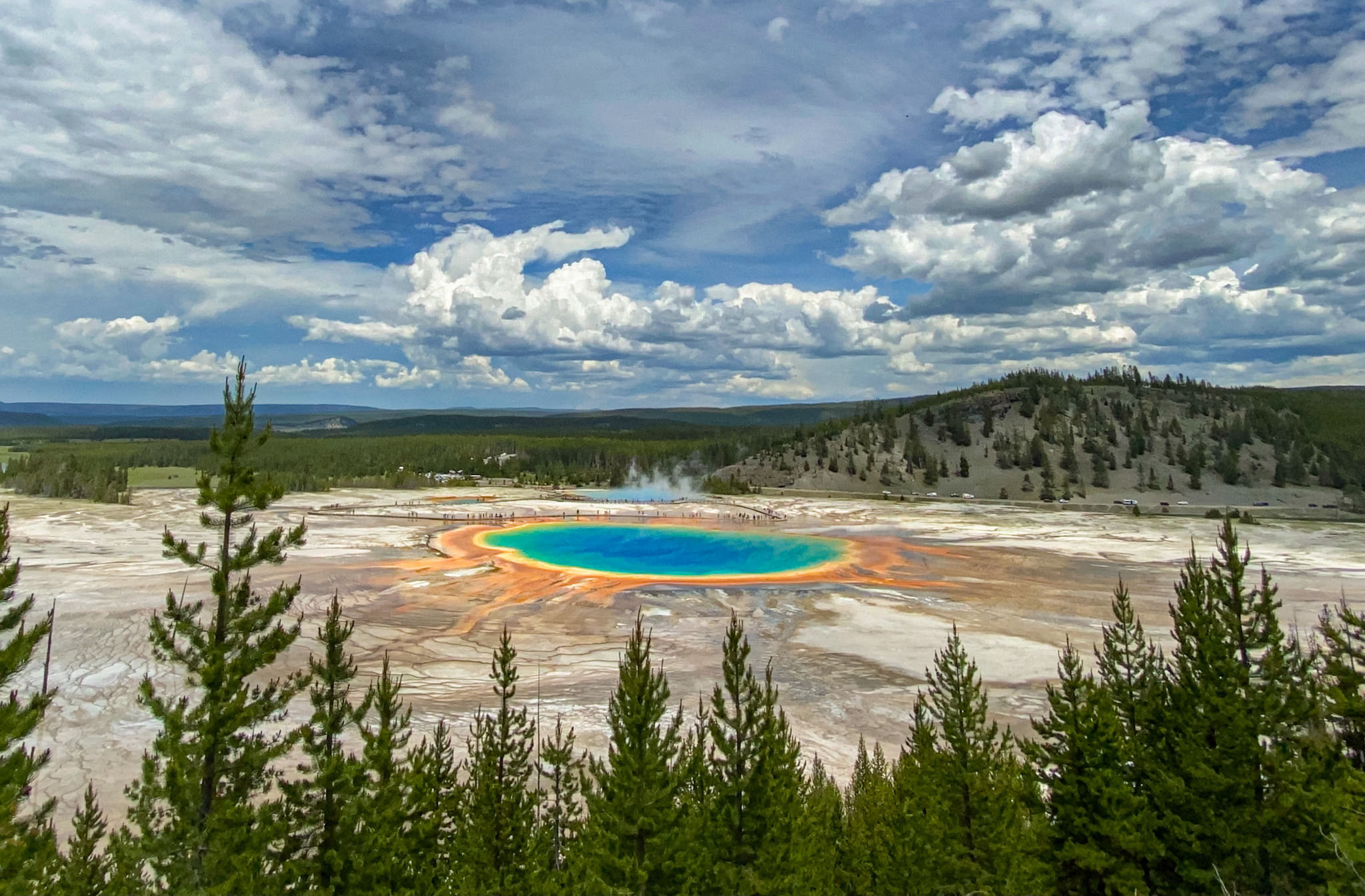 Basin of water surrounded by first, nothingness, then hills and tall trees. Around the basin is a ring of rainbow colors.